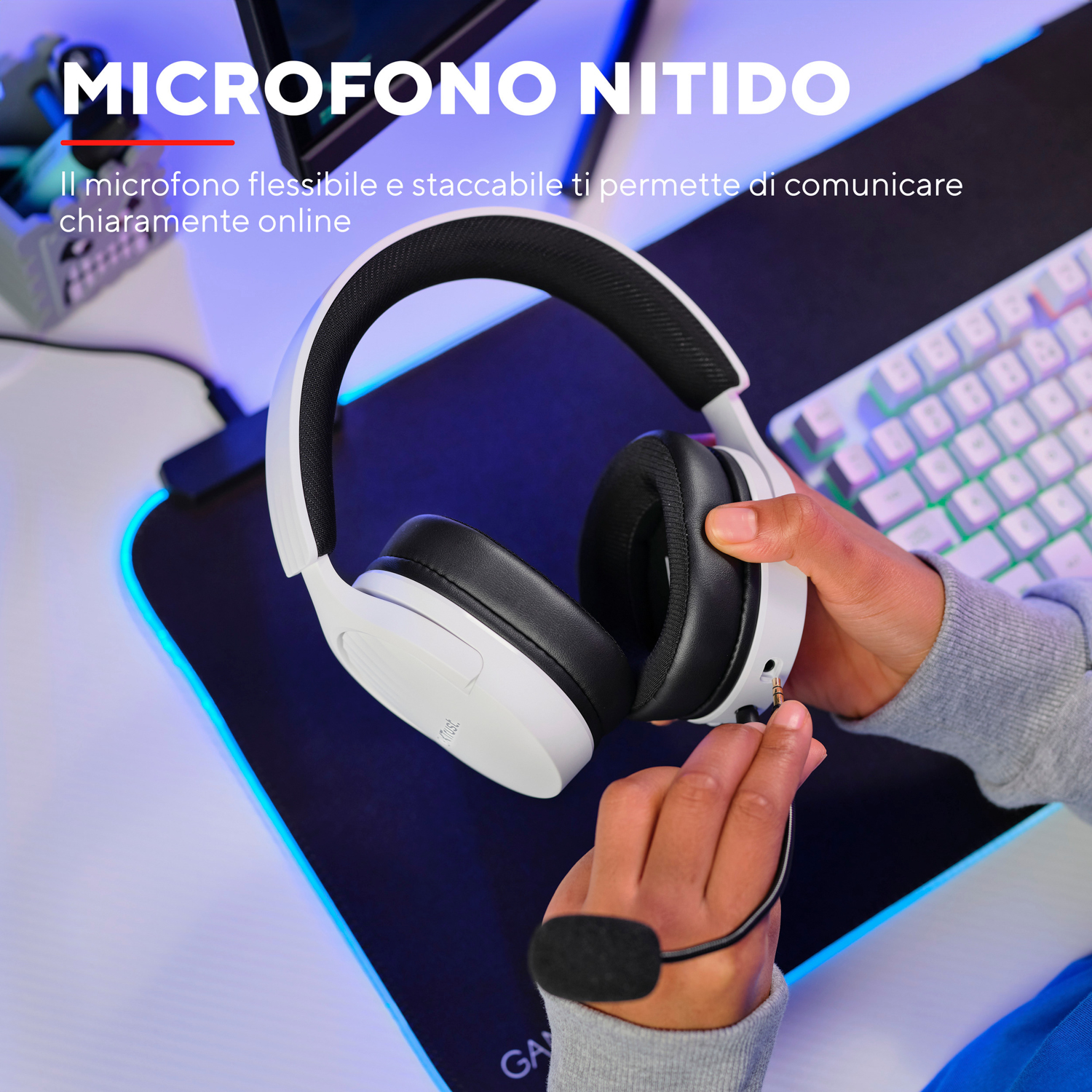 Persona che tiene cuffie bianche con microfono, configurazione da gioco con tastiera e tappetino.