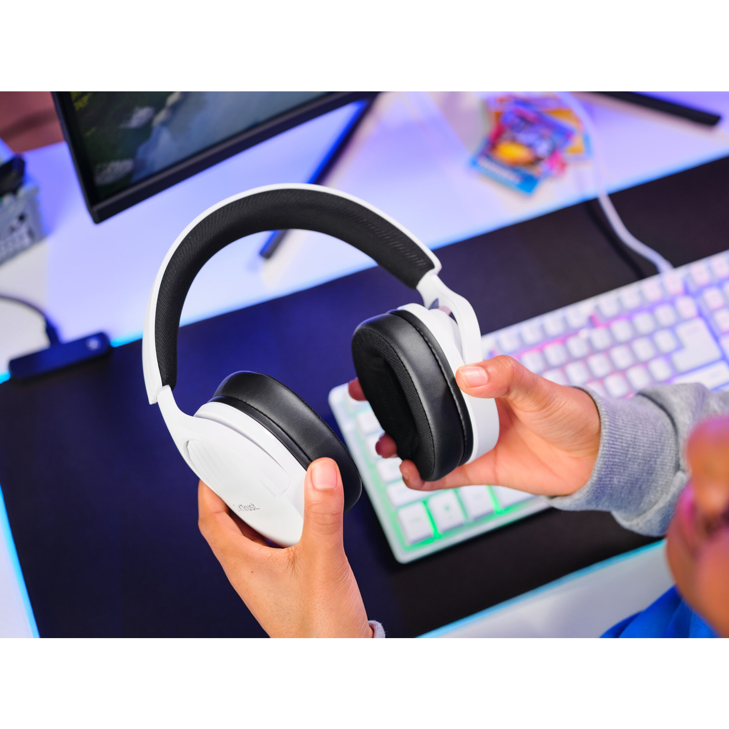 Persona che tiene un auricolare bianco e nero, con tastiera e monitor sullo sfondo.