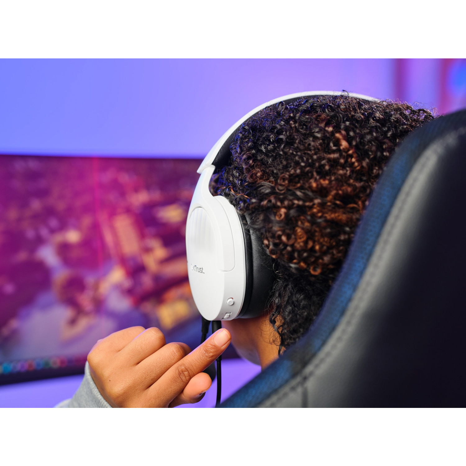 Una persona con cuffie bianche è concentrata su uno schermo di gioco. Lo sfondo è sfocato.