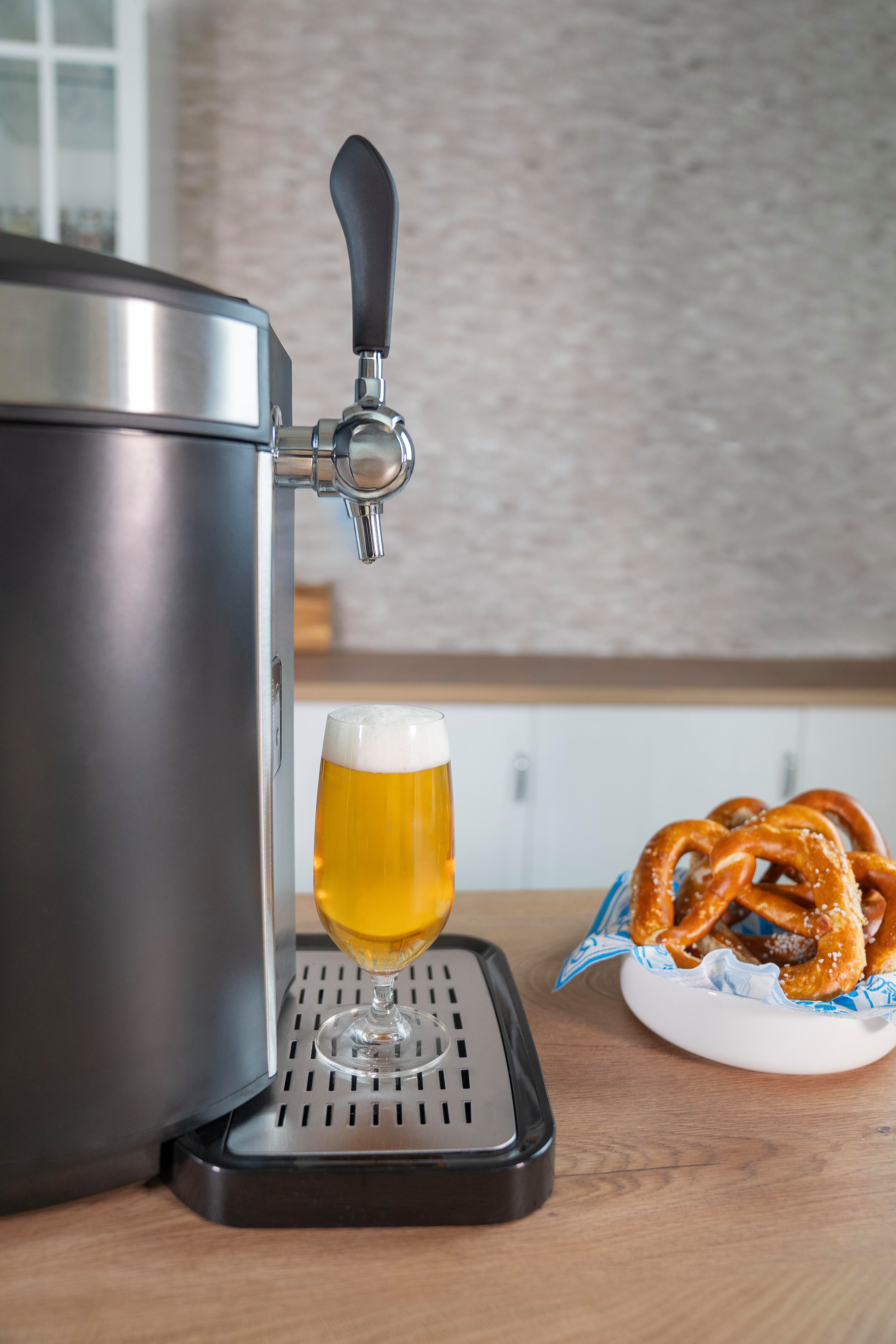 Ein Bierhahn mit einem Glas Bier und Brezeln auf einem Holztisch.