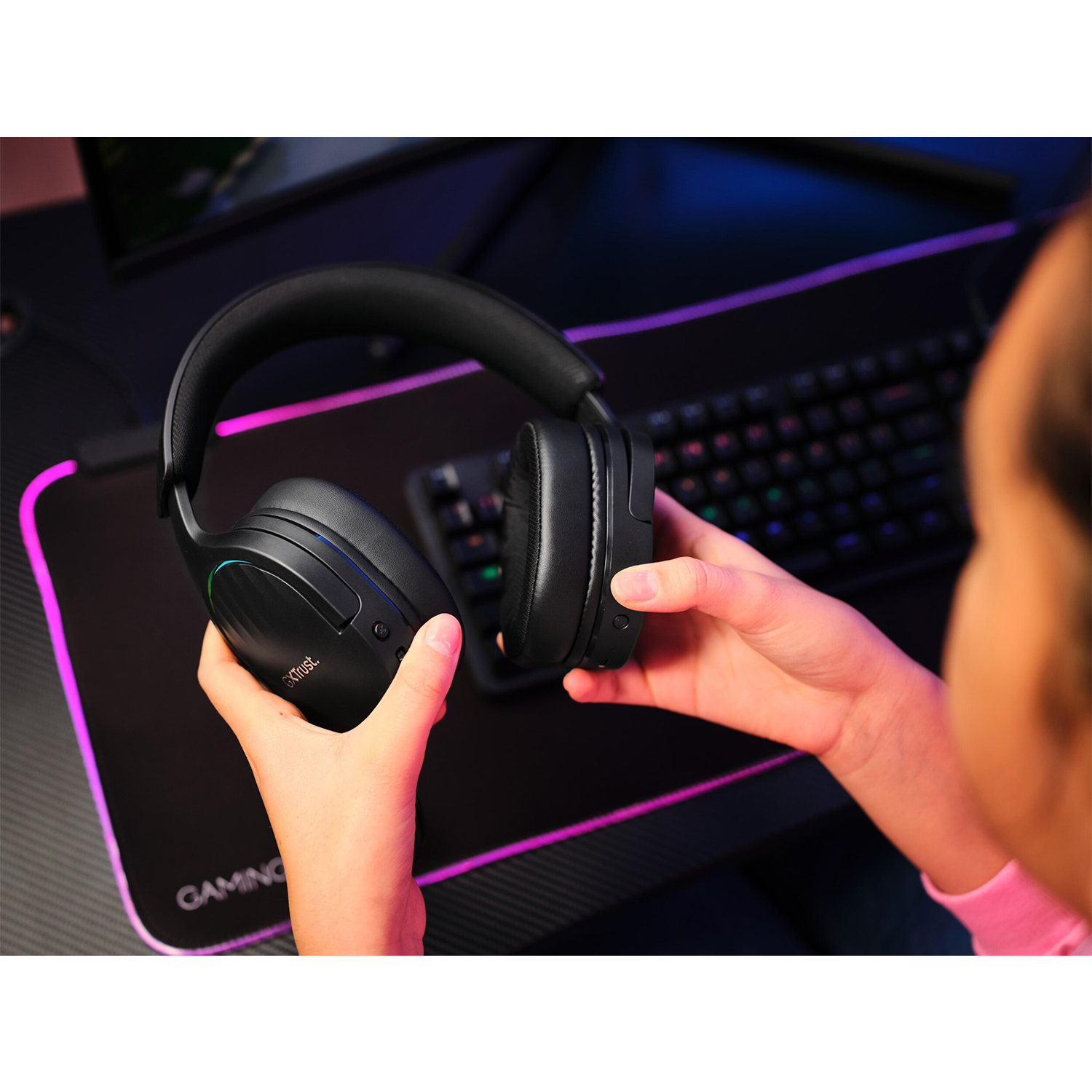 Cuffie nere tenute in mano, appoggiate su un mousepad e una tastiera.