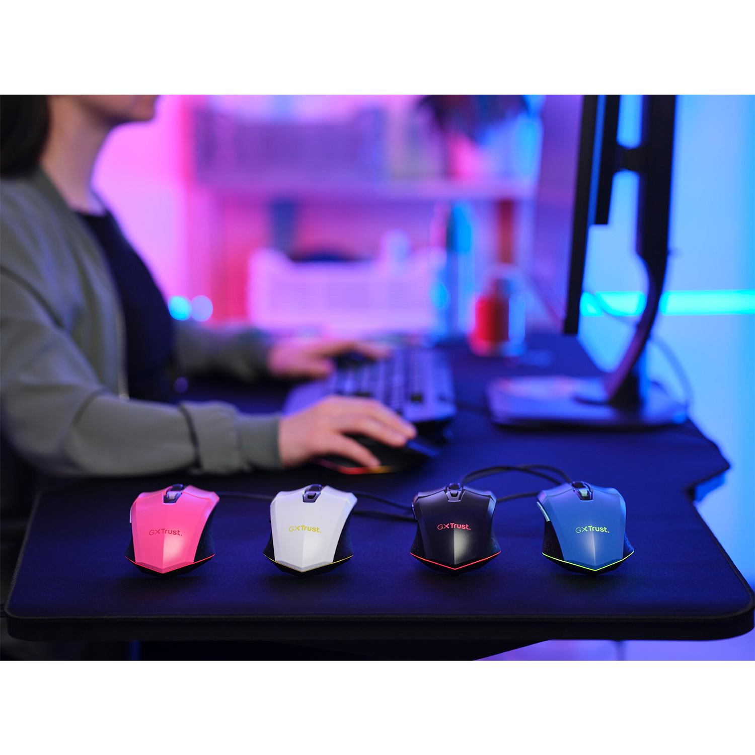 Quattro mouse da gioco di diversi colori su una superficie nera con un computer sullo sfondo.