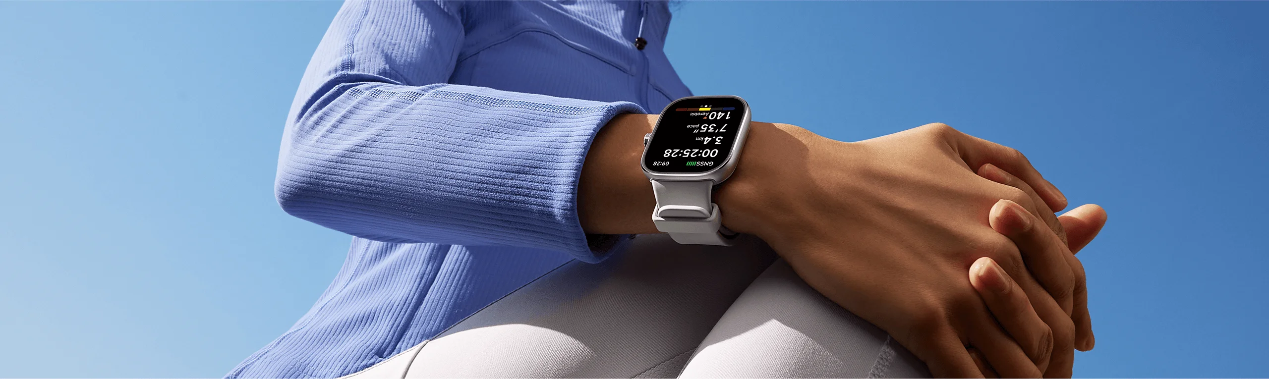 Polso di una persona con uno smartwatch bianco che mostra dati di fitness. Cielo blu sullo sfondo.