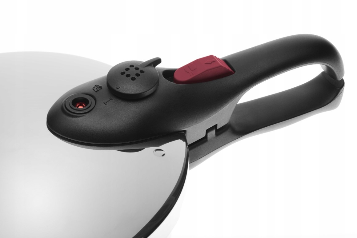 Zbliżenie pokrywy szybkowaru z czarnym uchwytem i czerwonym przyciskiem.