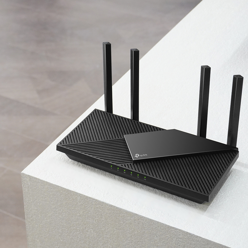 Fekete TP-Link Wi-Fi router négy antennával, fehér felületen zöld fényekkel.