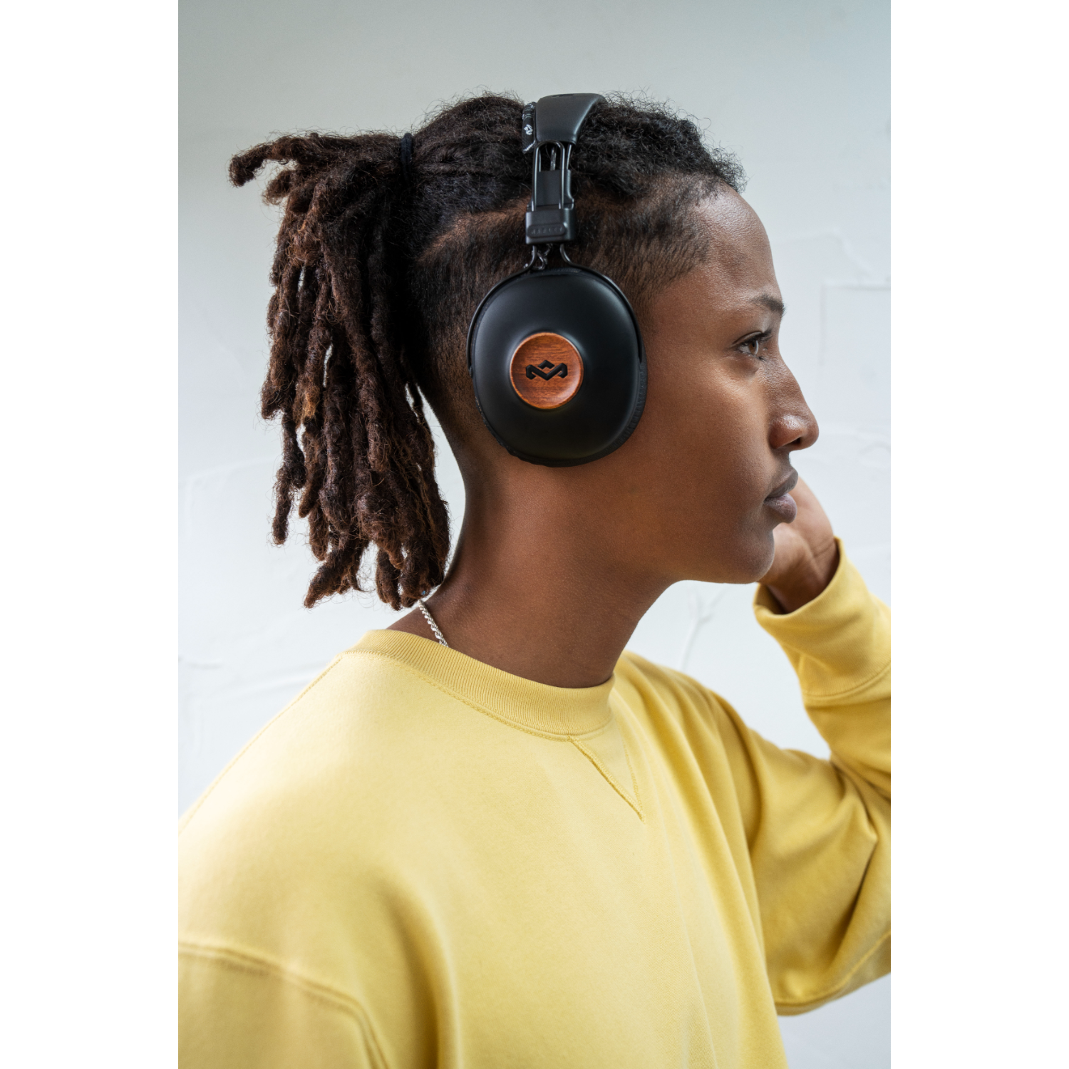 Persoon met dreadlocks draagt een koptelefoon met houten details. Ze dragen een gele trui.
