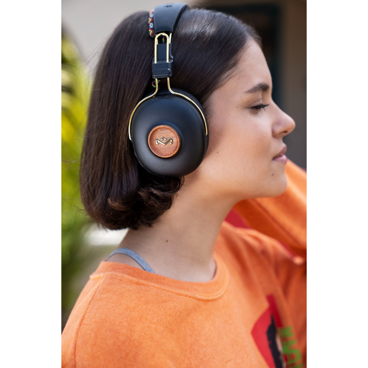 Woman wearing black headphones with gold accents. Background is blurred. 