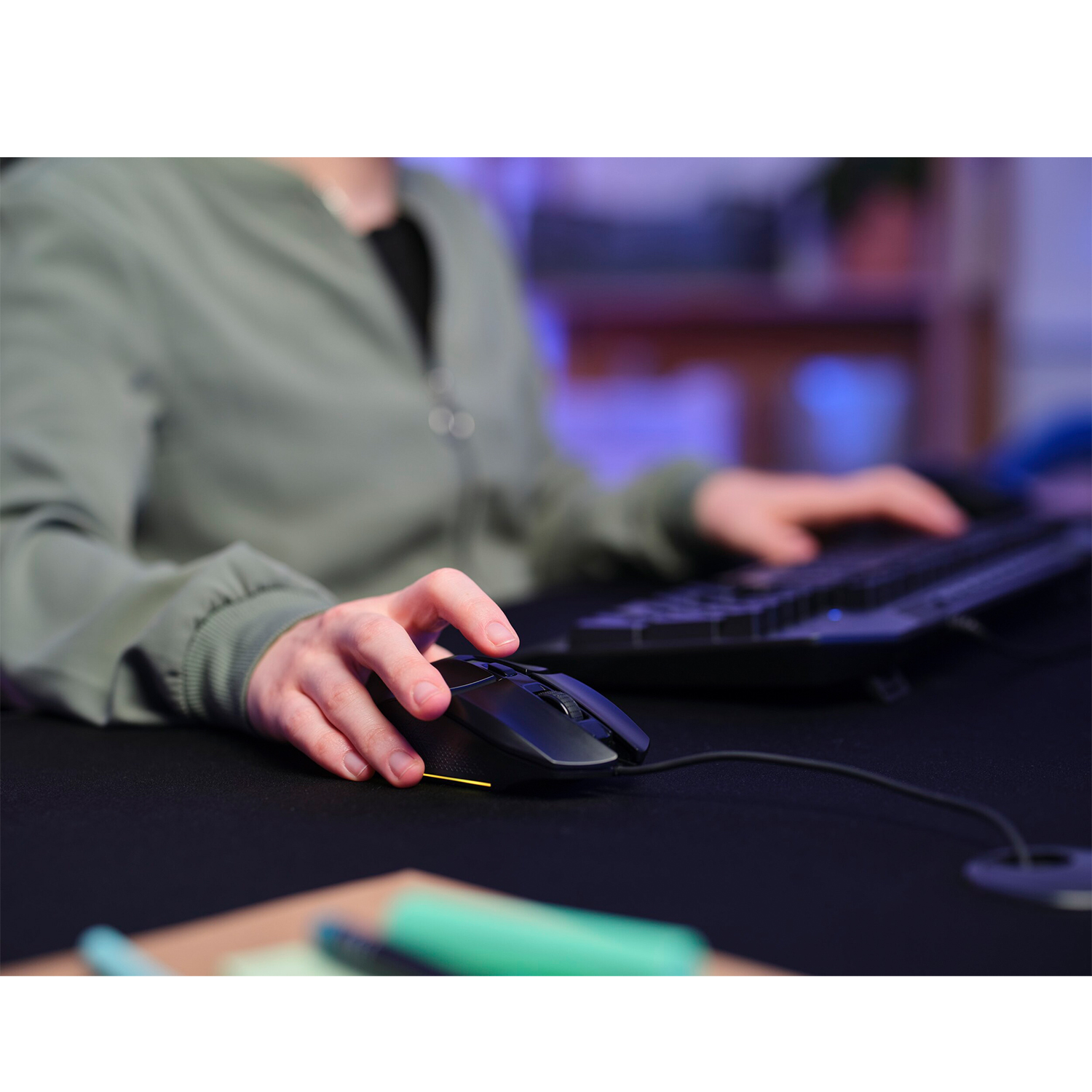 La mano di una persona è su un mouse nero con una tastiera nera sullo sfondo.