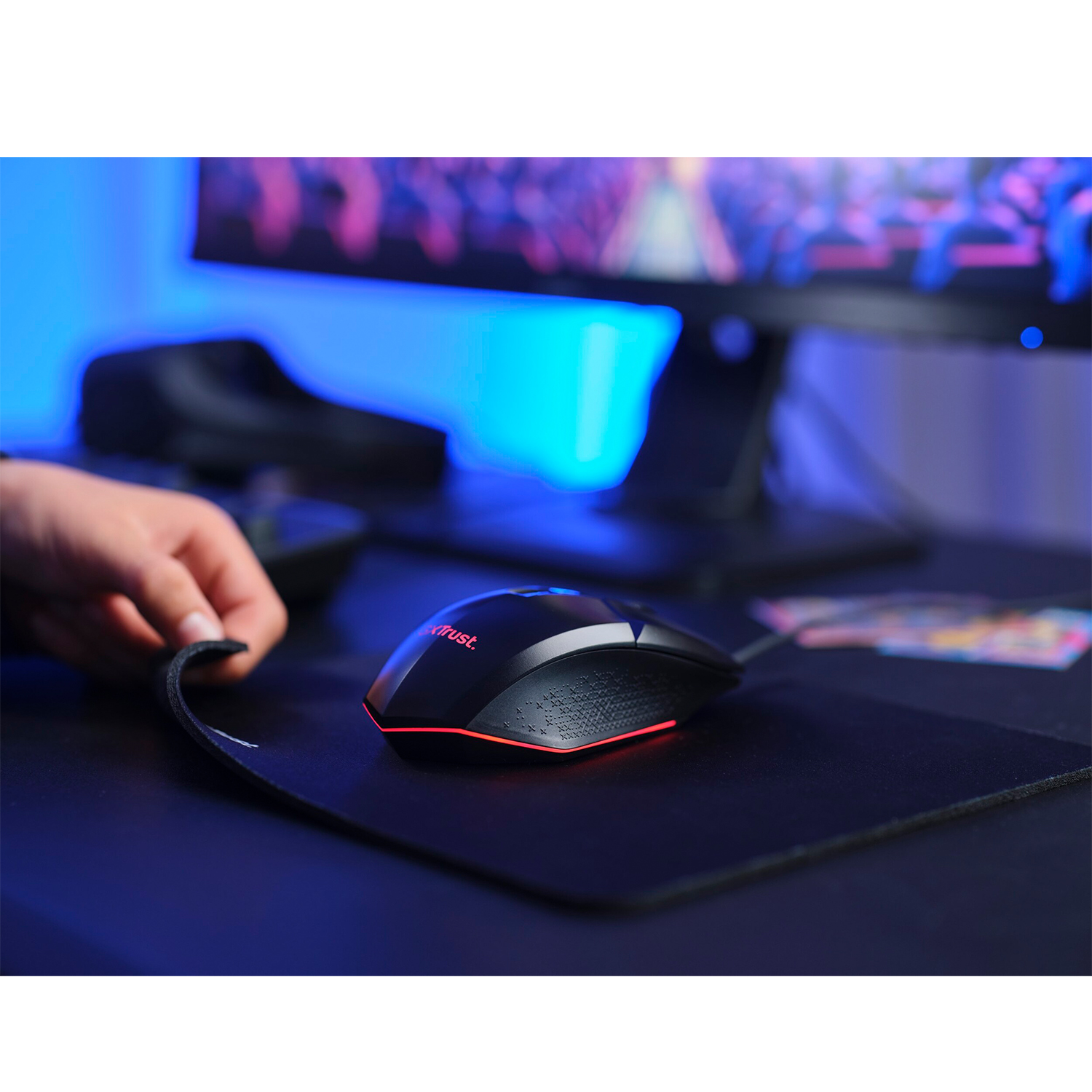 Un mouse da gioco nero con dettagli rossi è su un tappetino nero. Una mano tocca il tappetino.