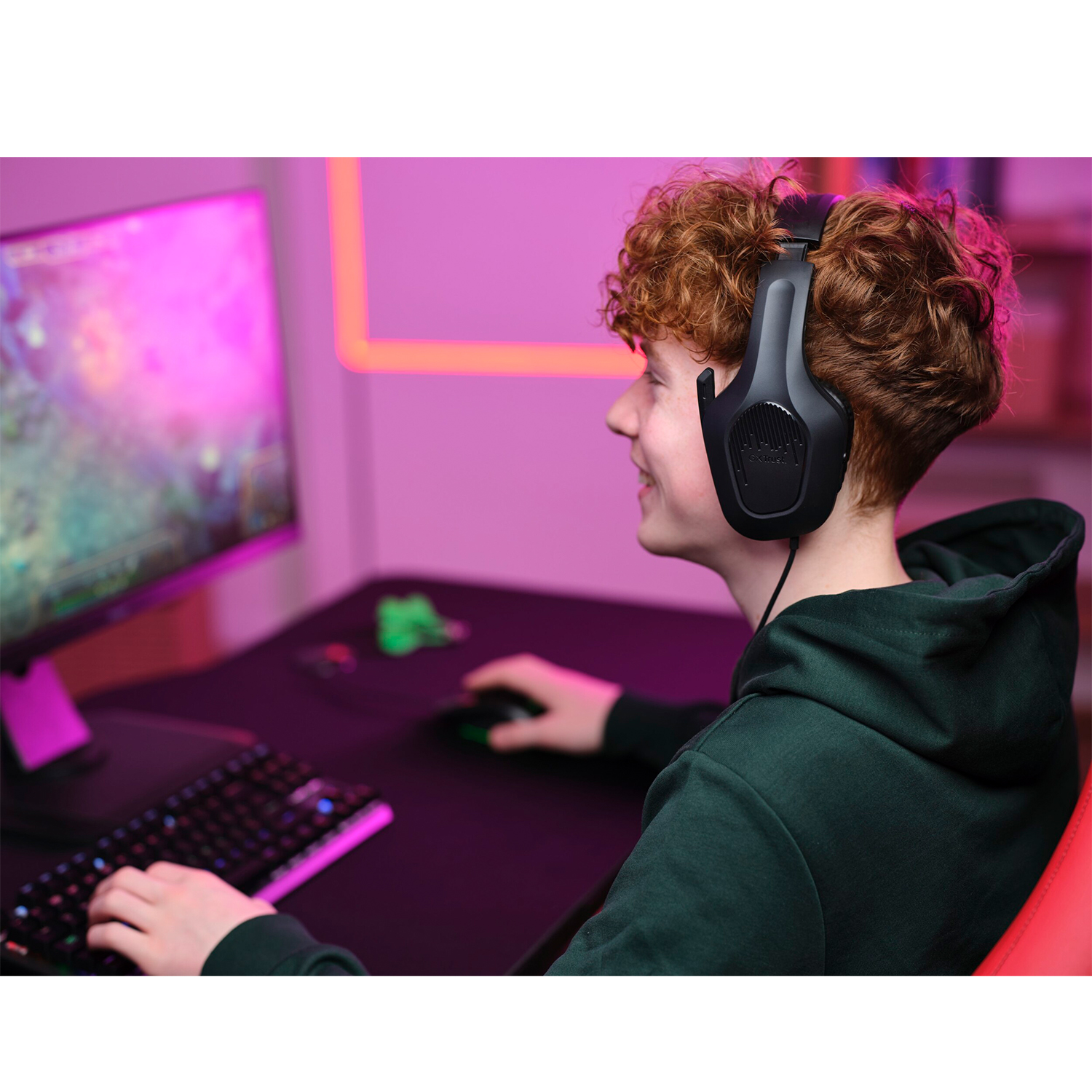 Adolescente con cuffie da gioco nere, sorridente allo schermo di un computer.