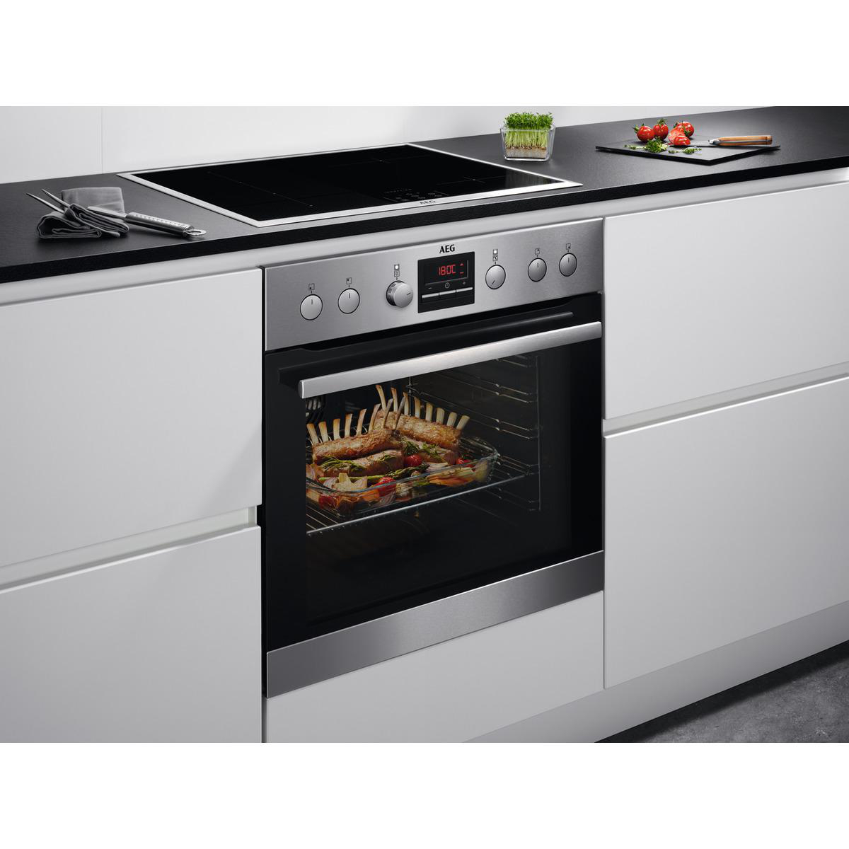 Ein Backofen mit Essen darin und ein Induktionskochfeld. Weiße Schränke umgeben die Szene.