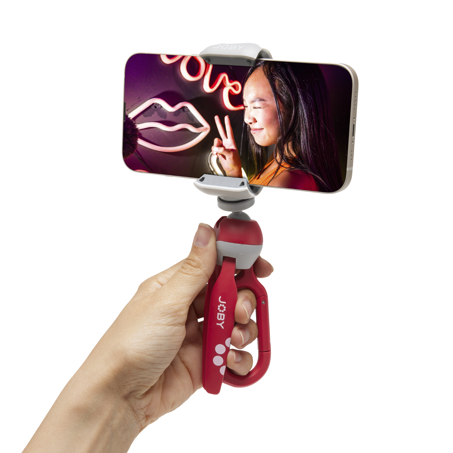 Een hand houdt een telefoon in een Joby-statief. De telefoon toont een vrouw voor een neonbord.