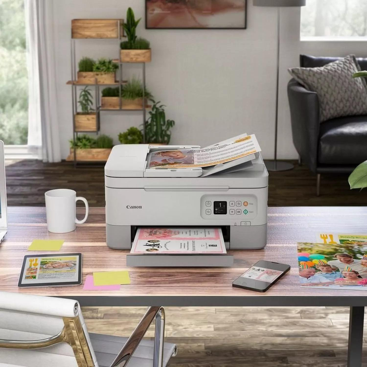 Ein Canon-Drucker mit bedruckten Seiten und einem Smartphone steht auf einem Holztisch.