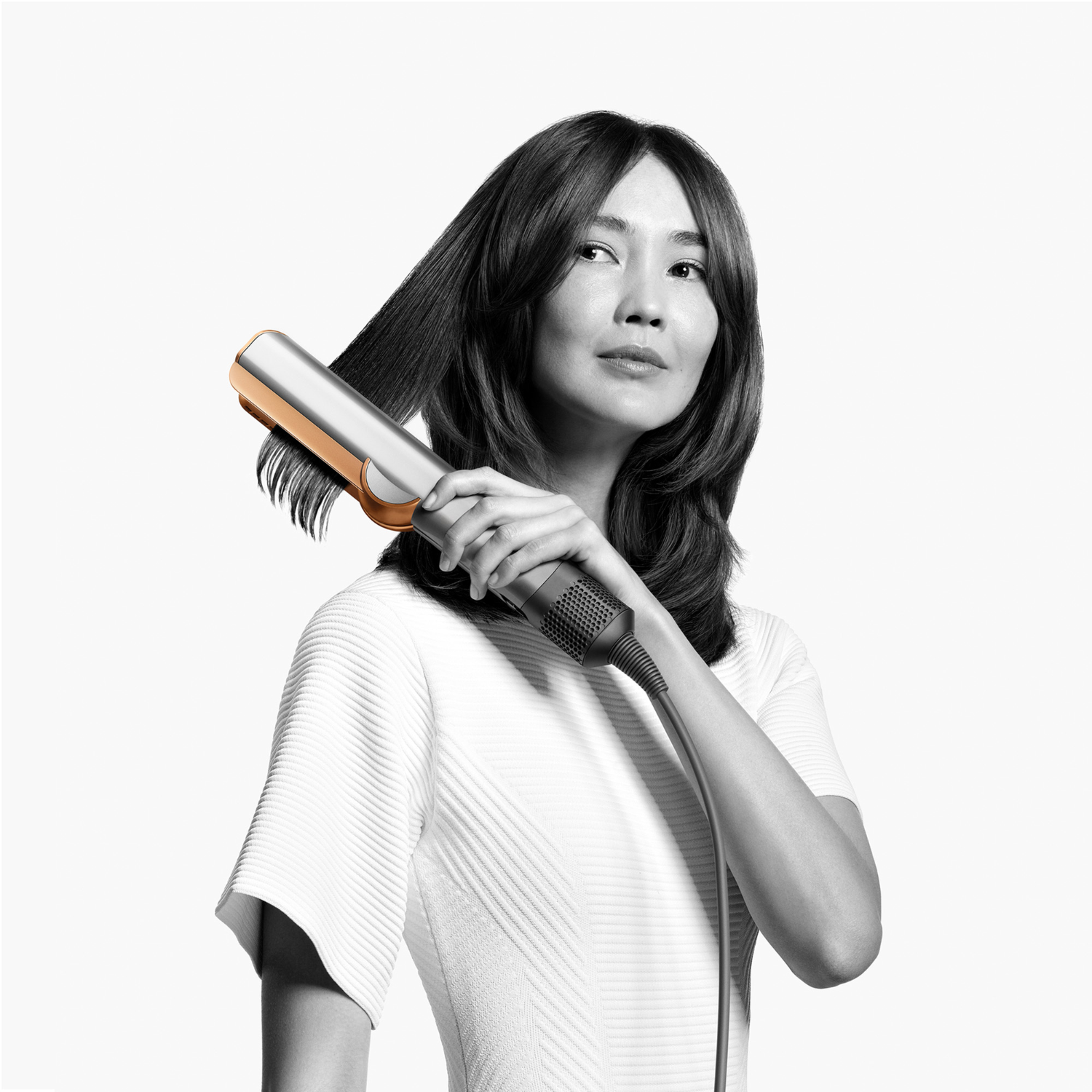 Woman styling her hair with a gold and silver straightener.