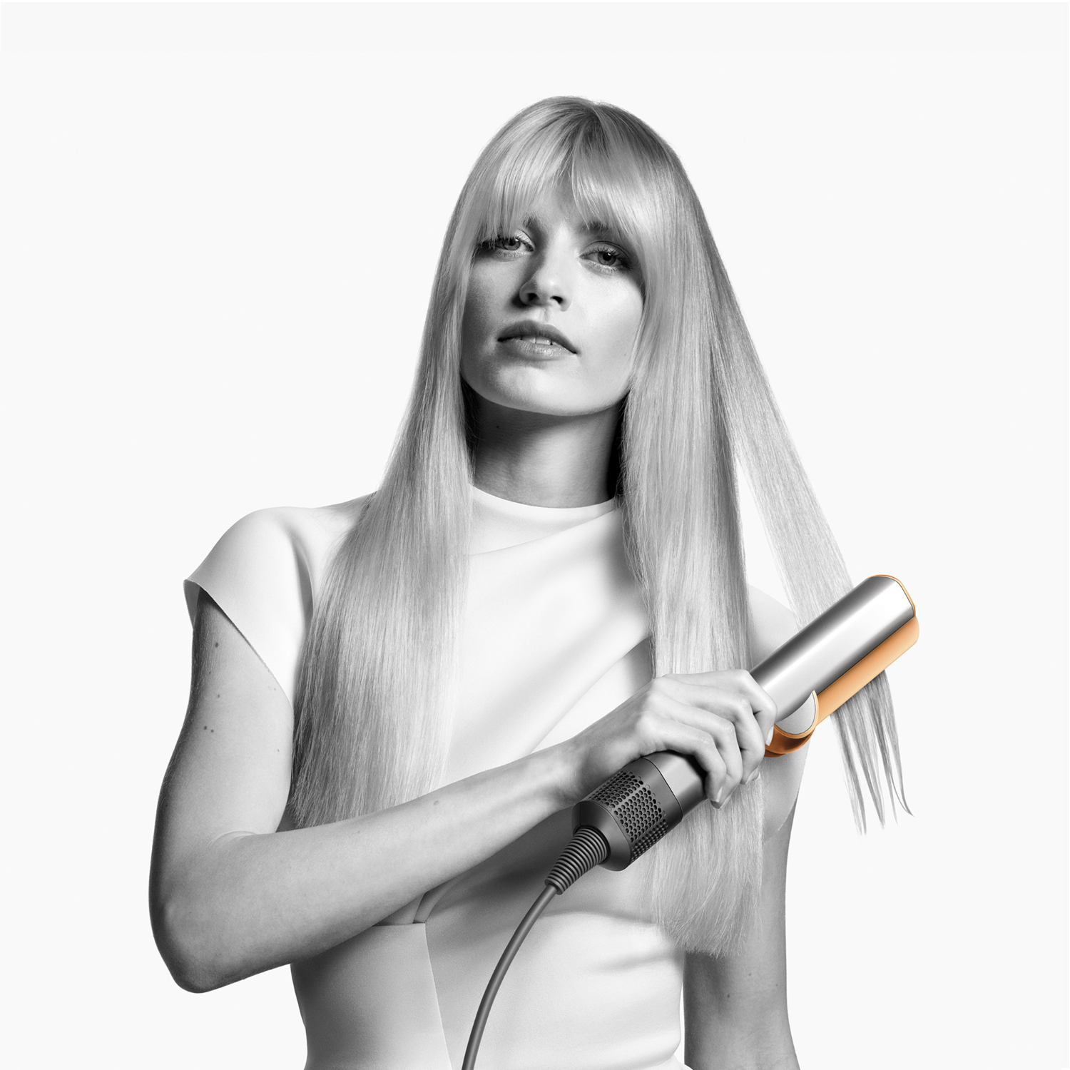 Woman with long blonde hair styling it with a black and gold hair styler.
