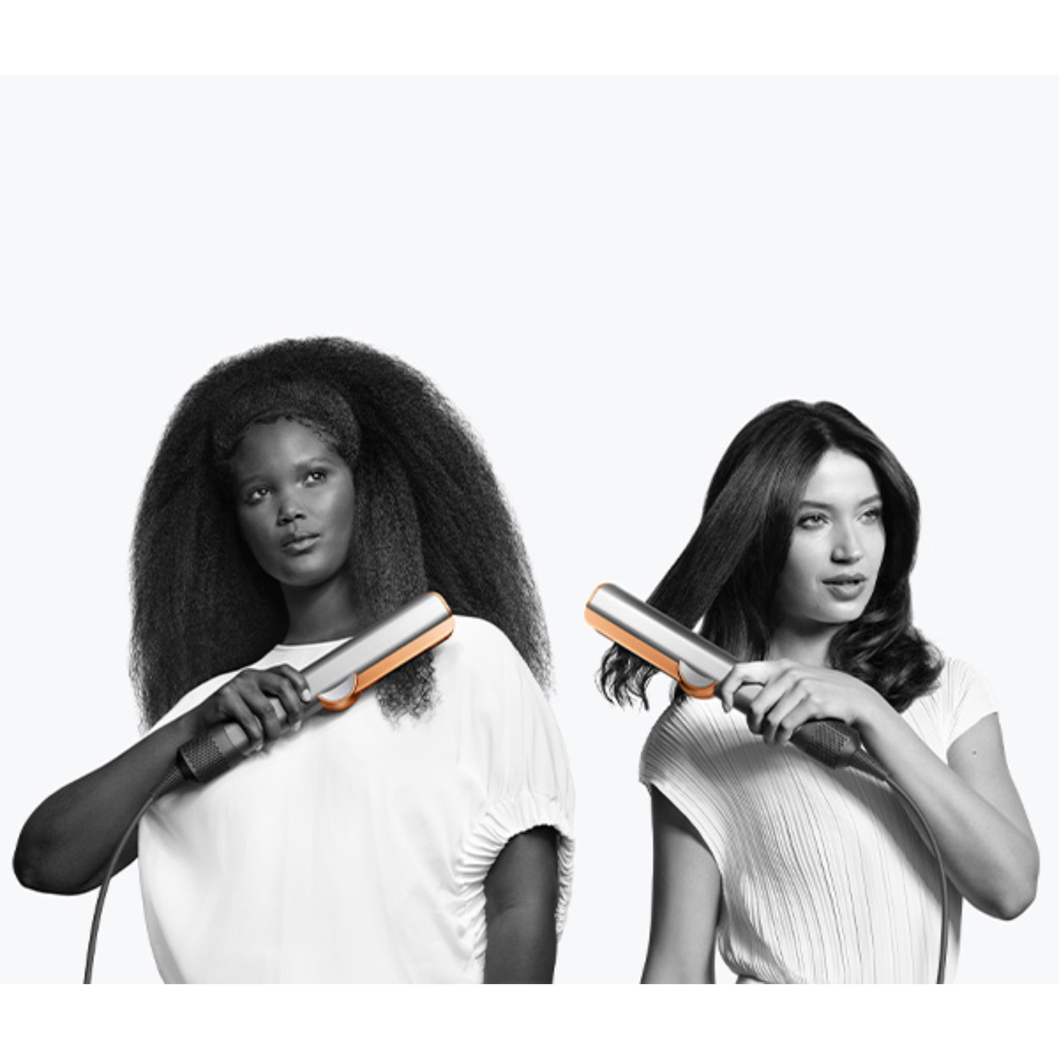 Two women using hair straighteners, one with curly hair and the other with straight hair, against white.