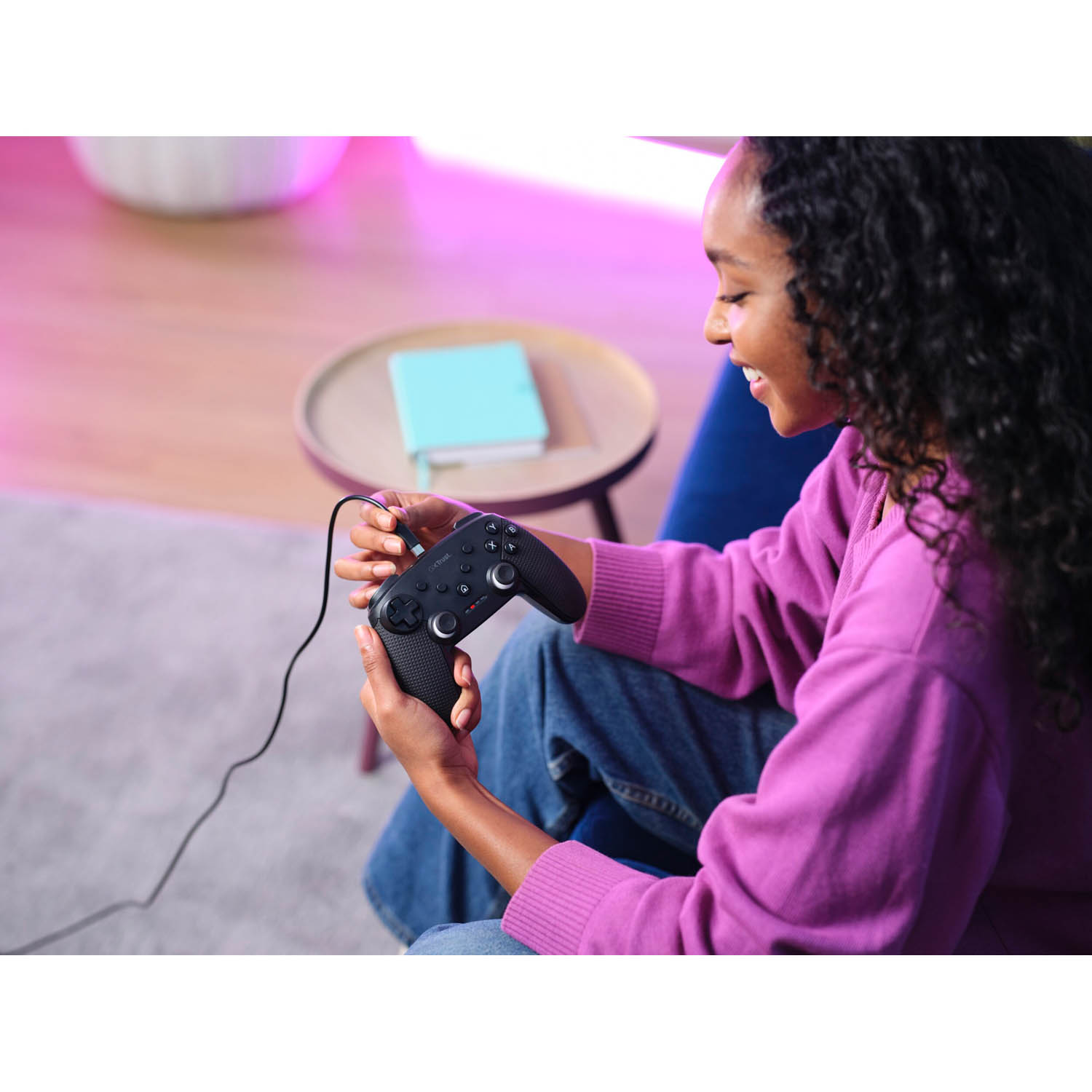 Donna che tiene in mano un controller di gioco nero, sorridente. È seduta su un divano blu.