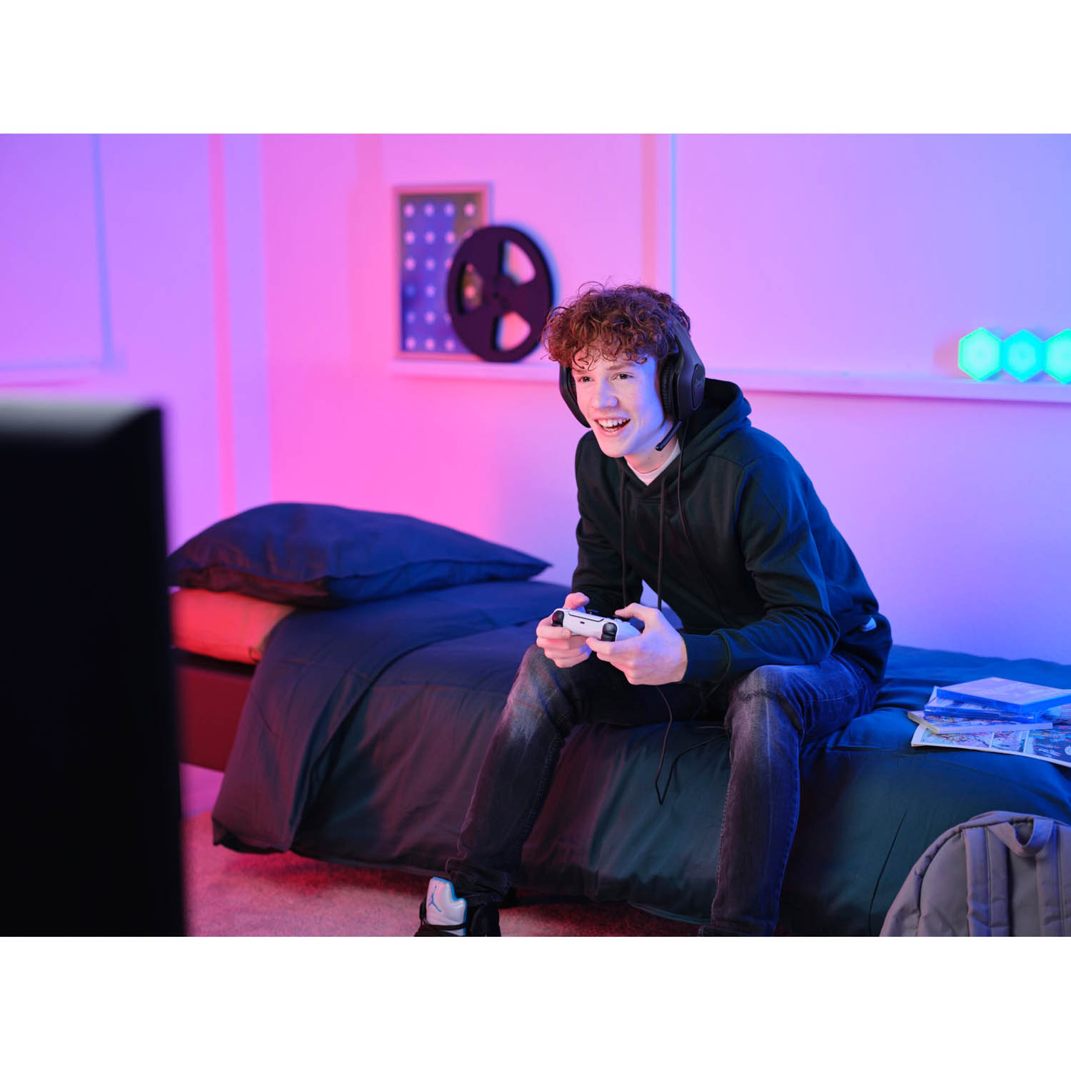 Un giovane sorride e gioca con un controller e delle cuffie in una stanza.