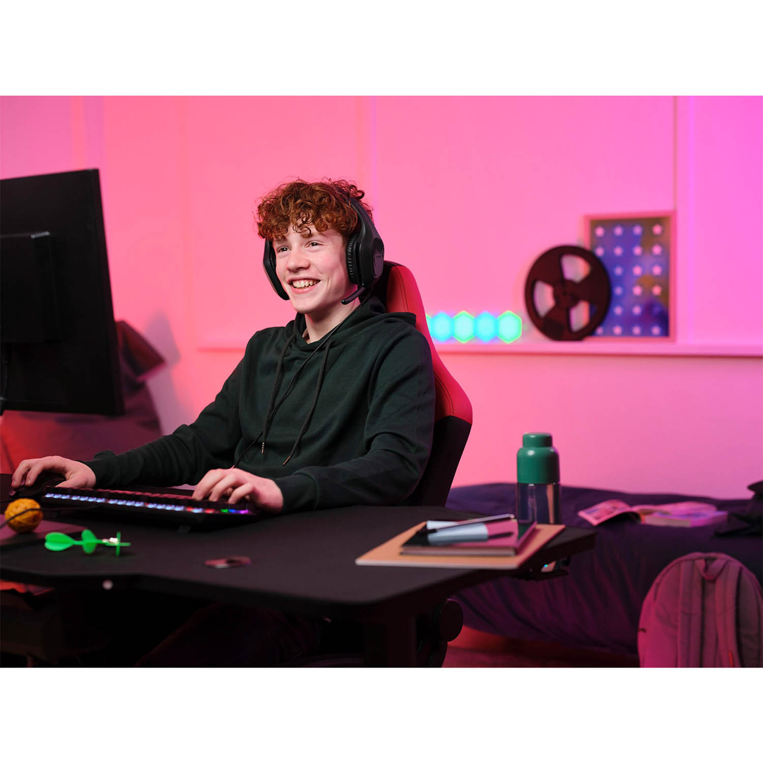 Un giovane giocatore con le cuffie, sorridente mentre usa un computer con una sedia da gioco rossa.