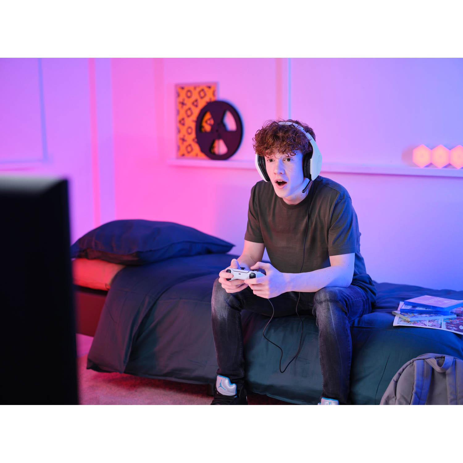 Un adolescente gioca a un videogioco, sembra eccitato. Tiene in mano un controller, con un monitor davanti.