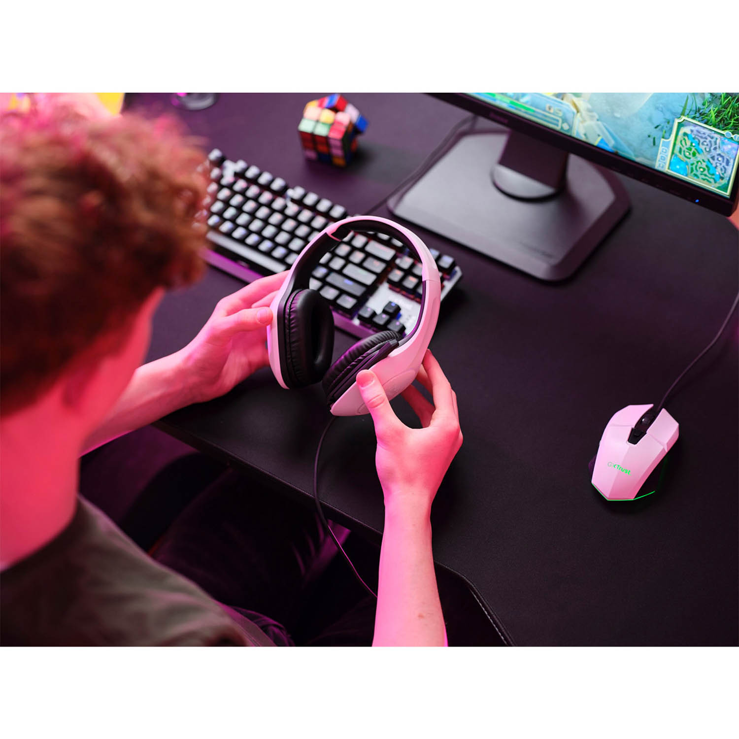 Persona che tiene cuffie rosa vicino a una configurazione computer.
