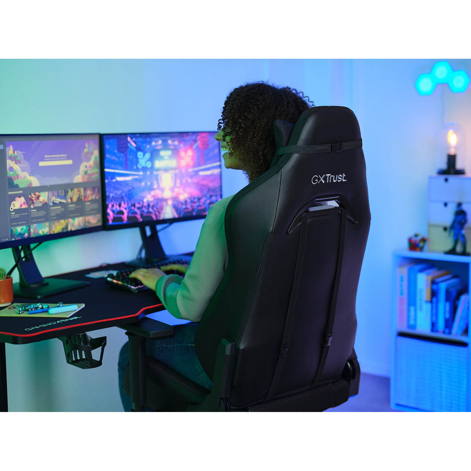 Un giocatore seduto su una sedia GX Trust nera, che gioca su due monitor.