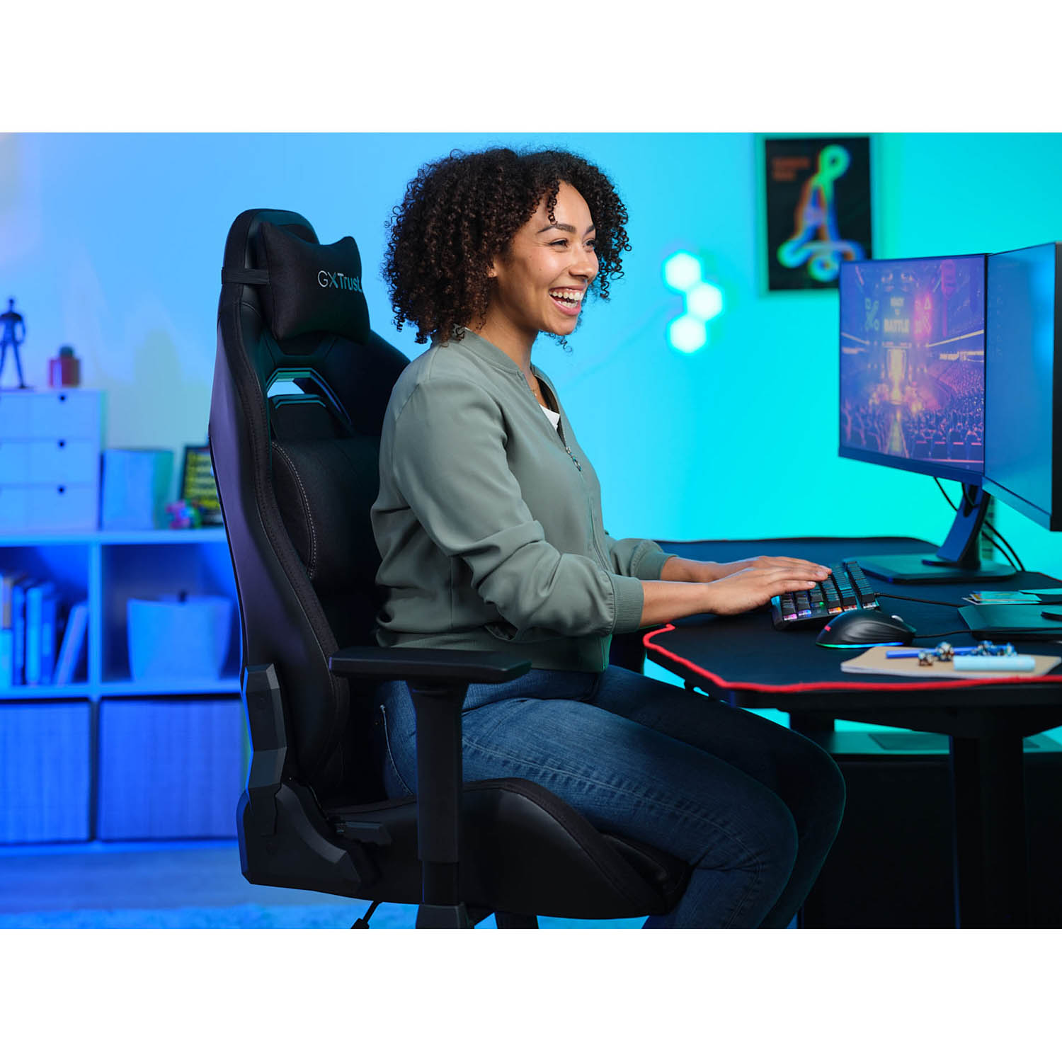 Donna sorridente mentre gioca al computer. Indossa una giacca verde e siede su una sedia da gaming nera.
