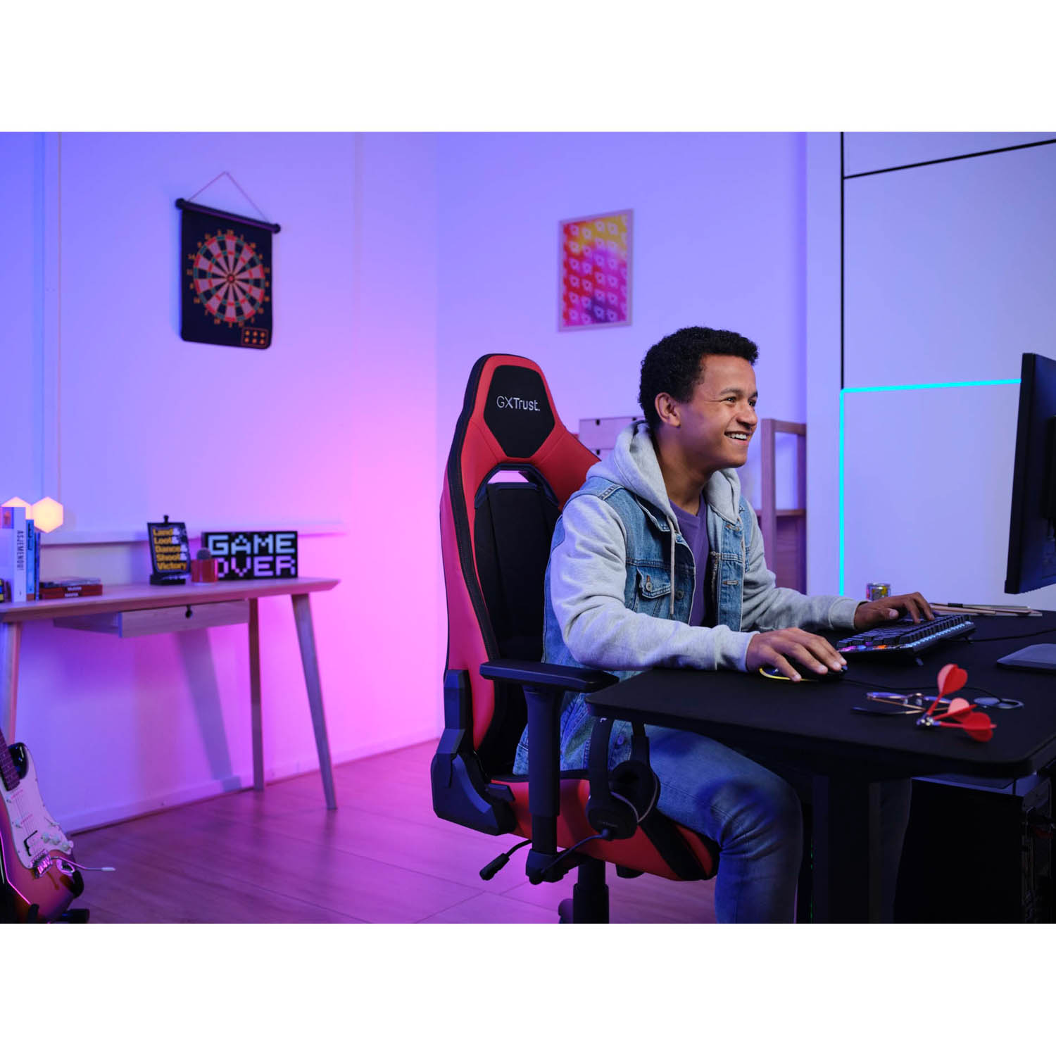 Un giovane sorride al computer mentre gioca. È su una sedia da gaming rossa e nera.