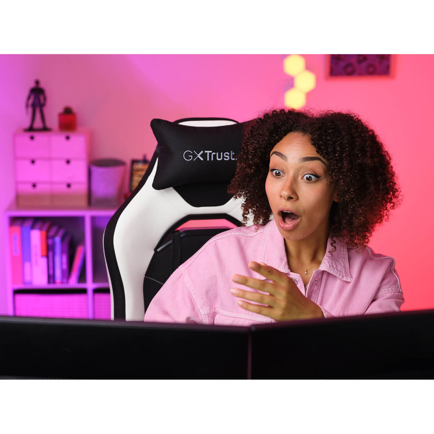 Donna con i capelli ricci sorpresa. Seduta su sedia gaming bianca e nera, guarda uno schermo.