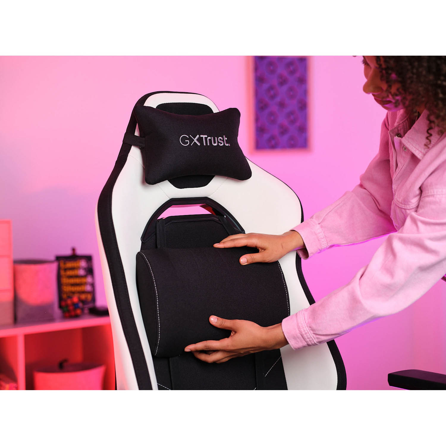 Donna che posiziona un poggiatesta nero su una sedia da gaming. Sedia bianca e nera, sfondo rosa.