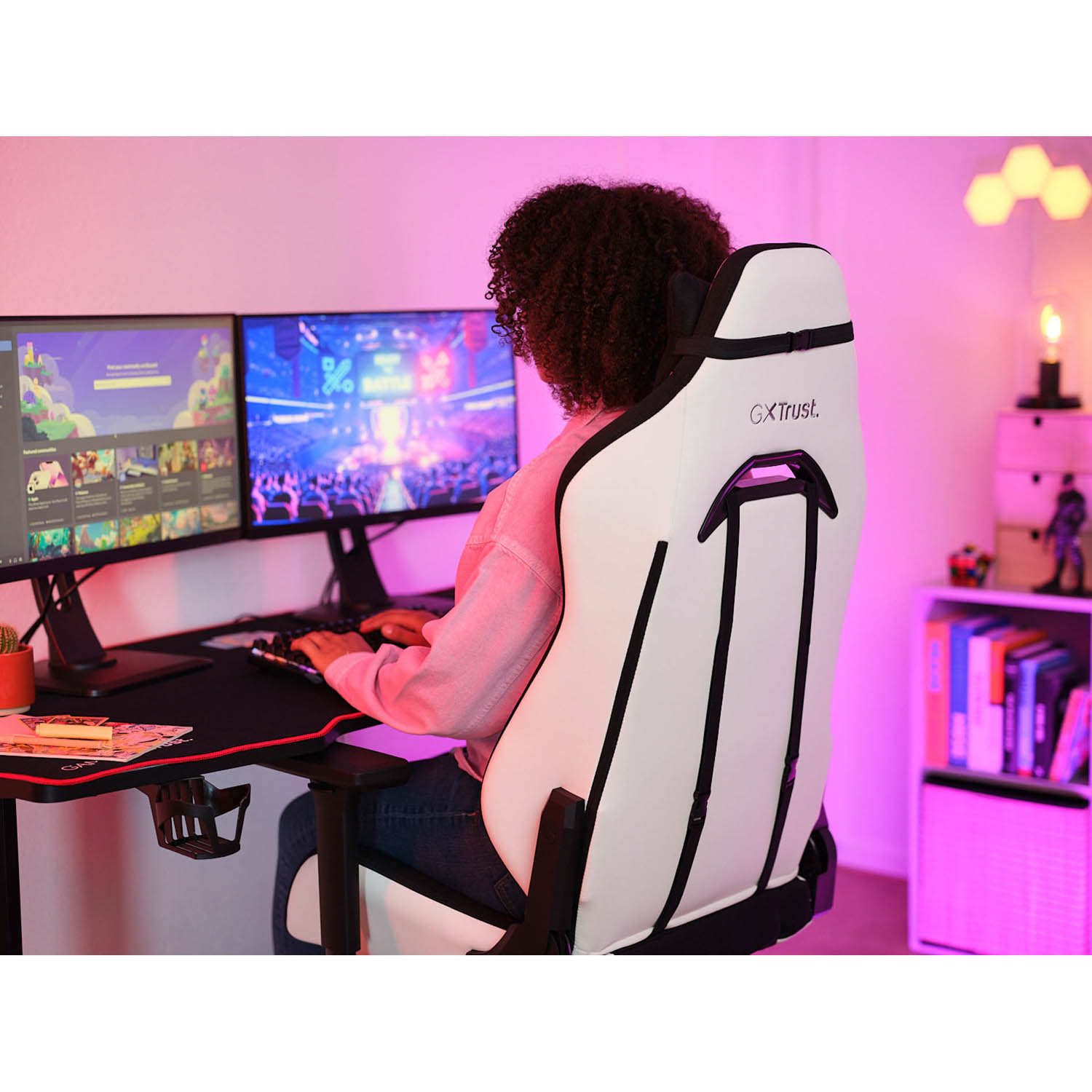 Persona seduta su una sedia da gaming bianca e nera, di fronte a due monitor di computer. Una scrivania e scaffali sullo sfondo.