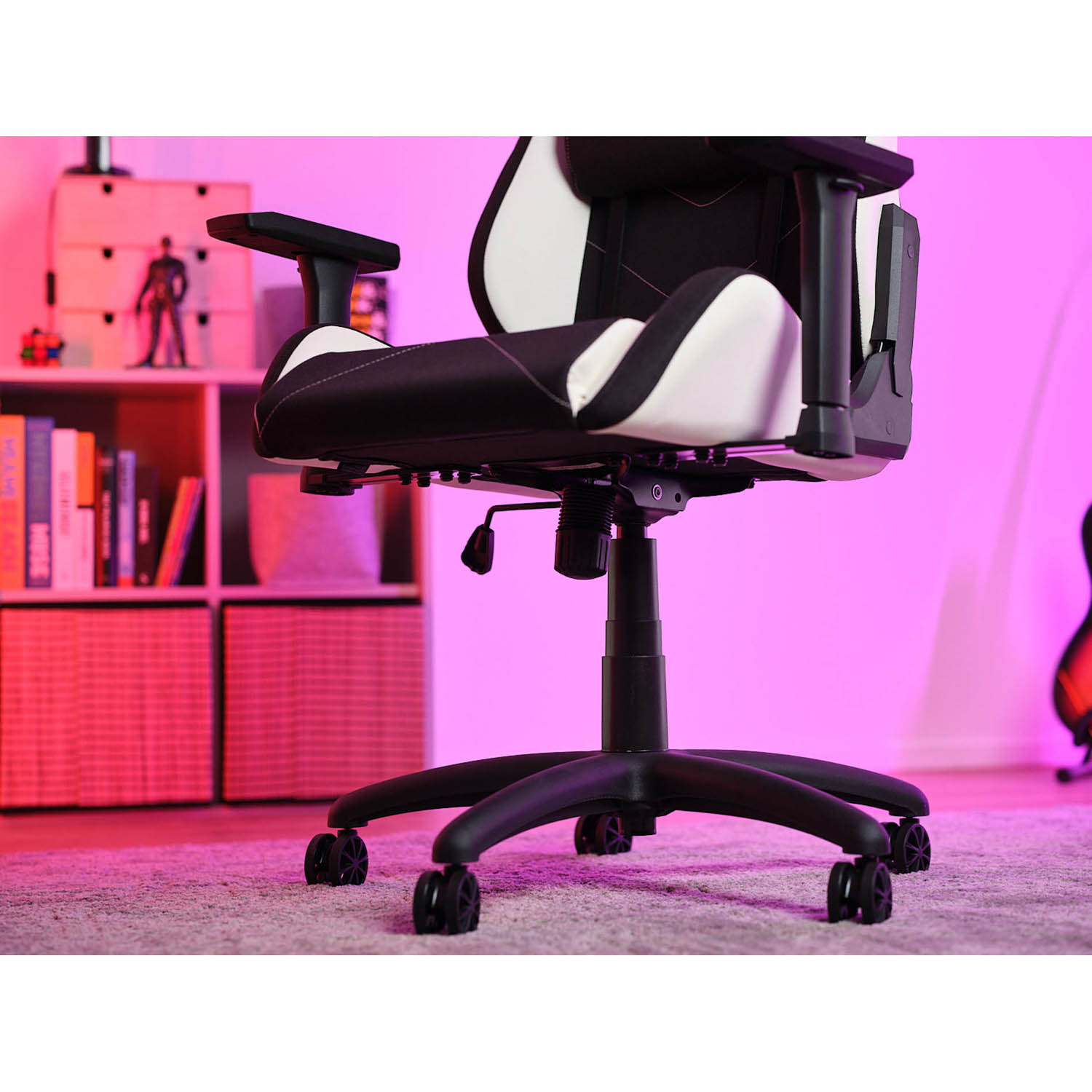 Una sedia da gaming è in una stanza con illuminazione rosa e viola, una libreria e un monitor.