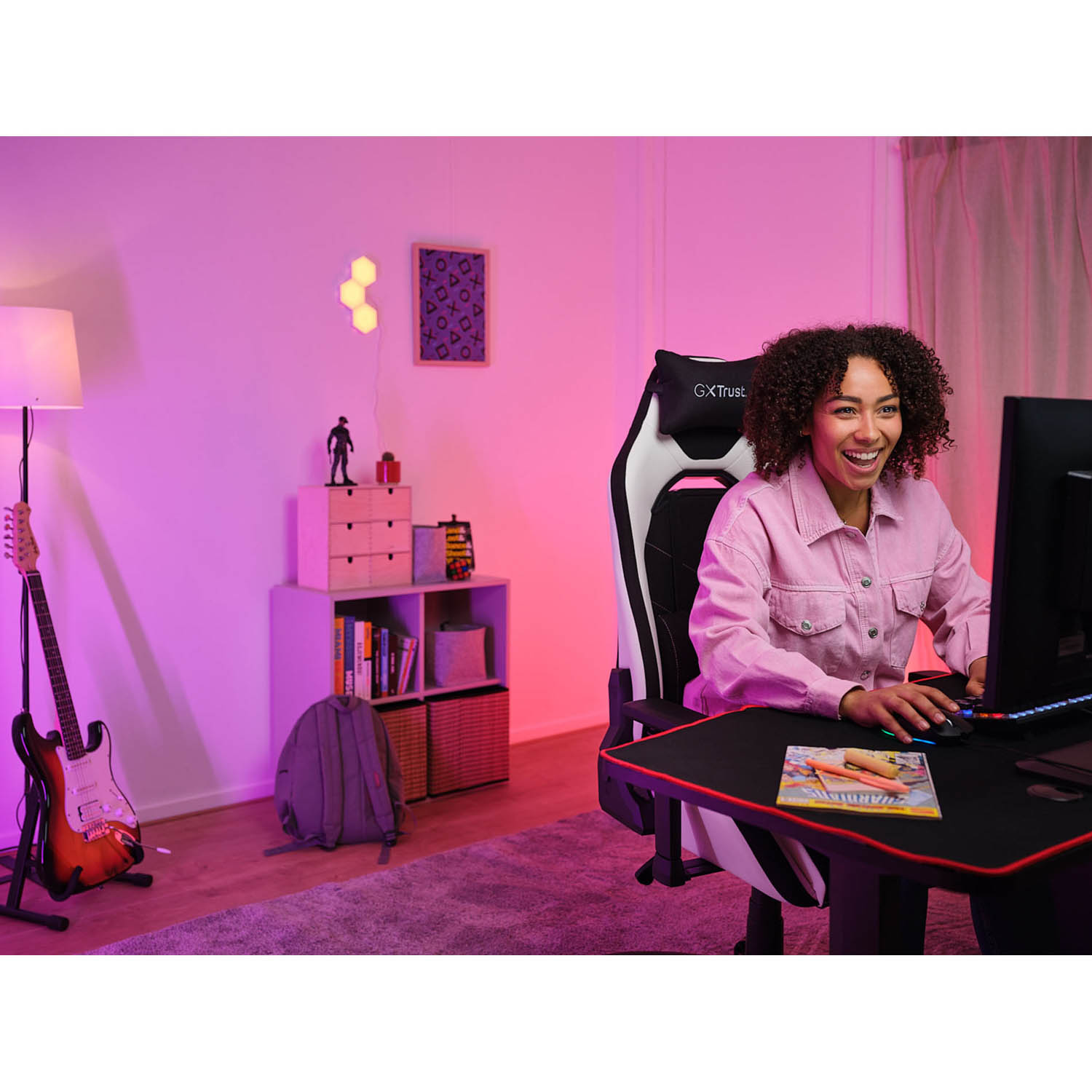 Una donna sorride mentre usa un computer. È su una sedia da gioco. La stanza ha una luce rosa.