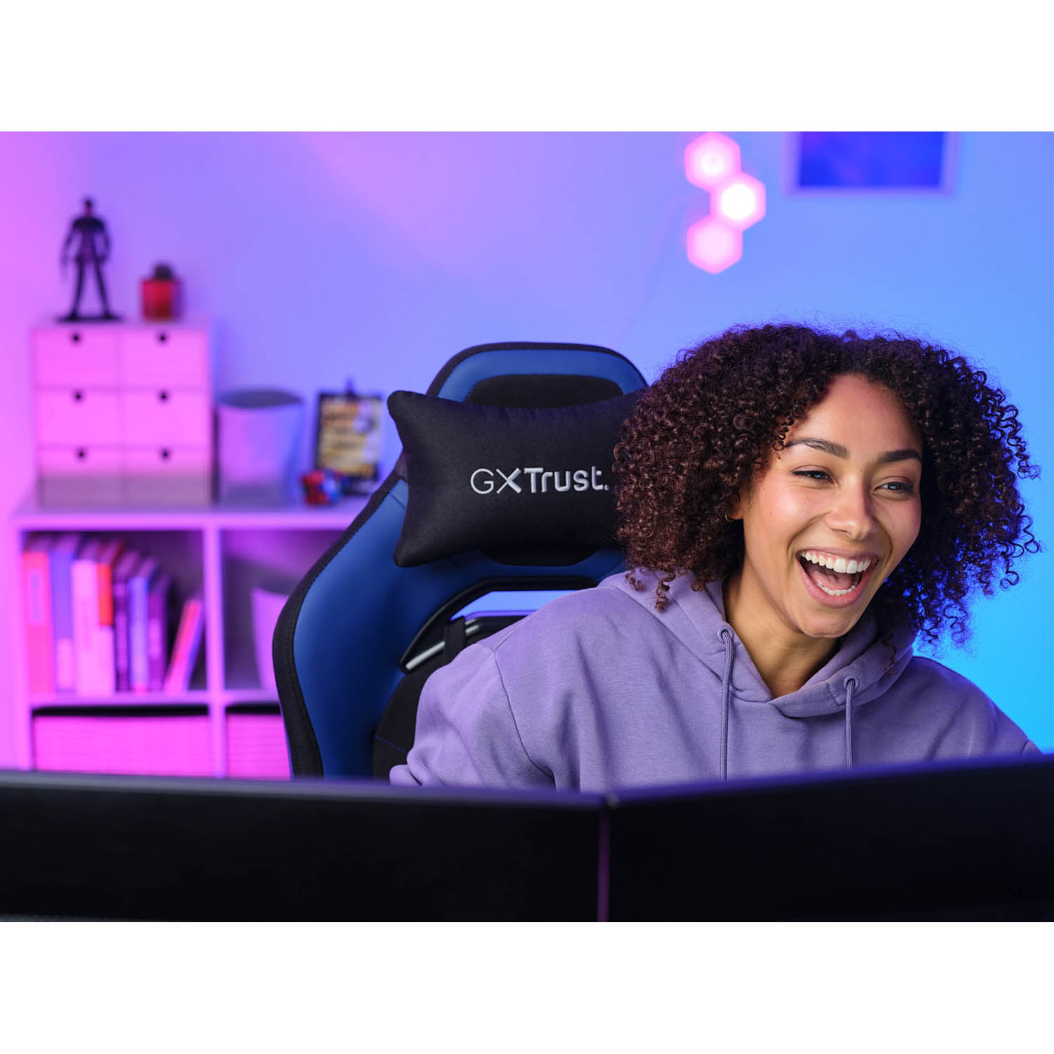 Una donna sorride seduta su una sedia da gioco, con un monitor dietro di lei.