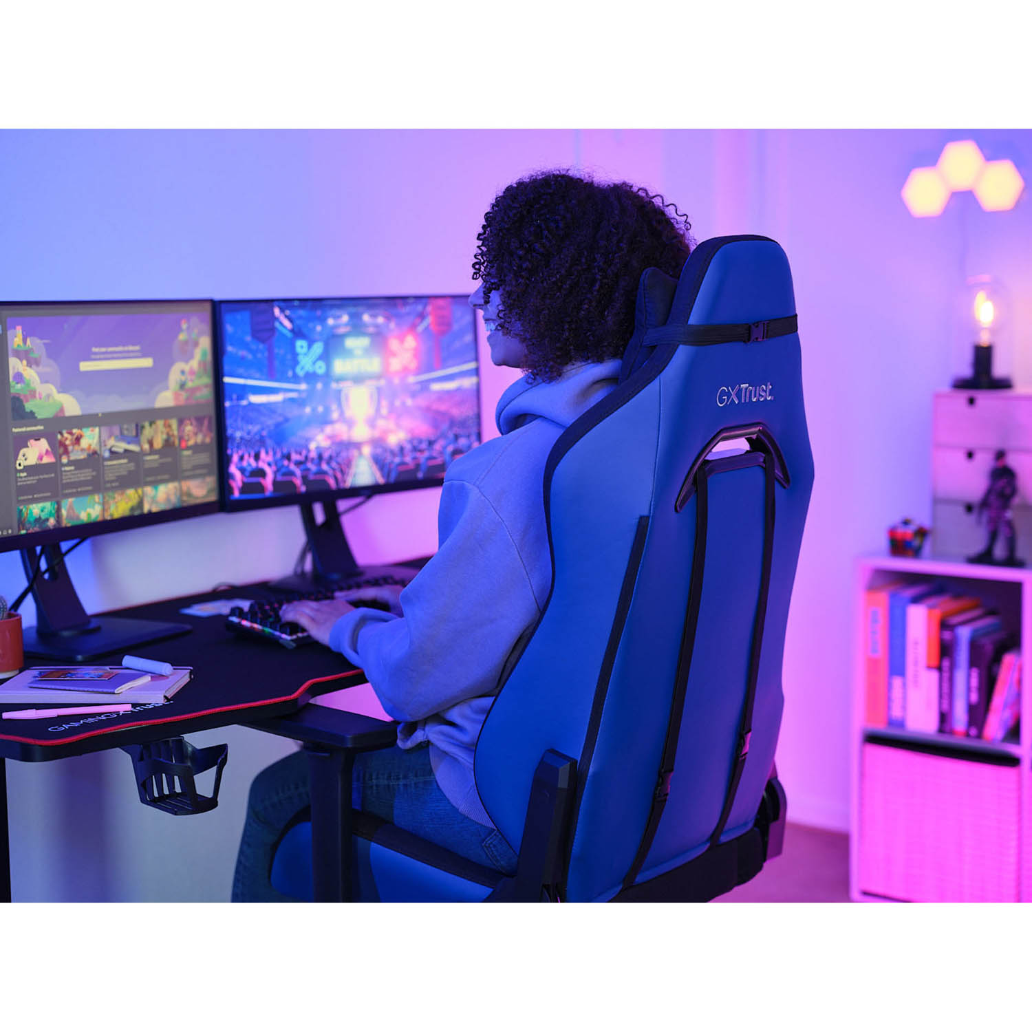 Persona su una sedia da gaming blu con due monitor e una tastiera.
