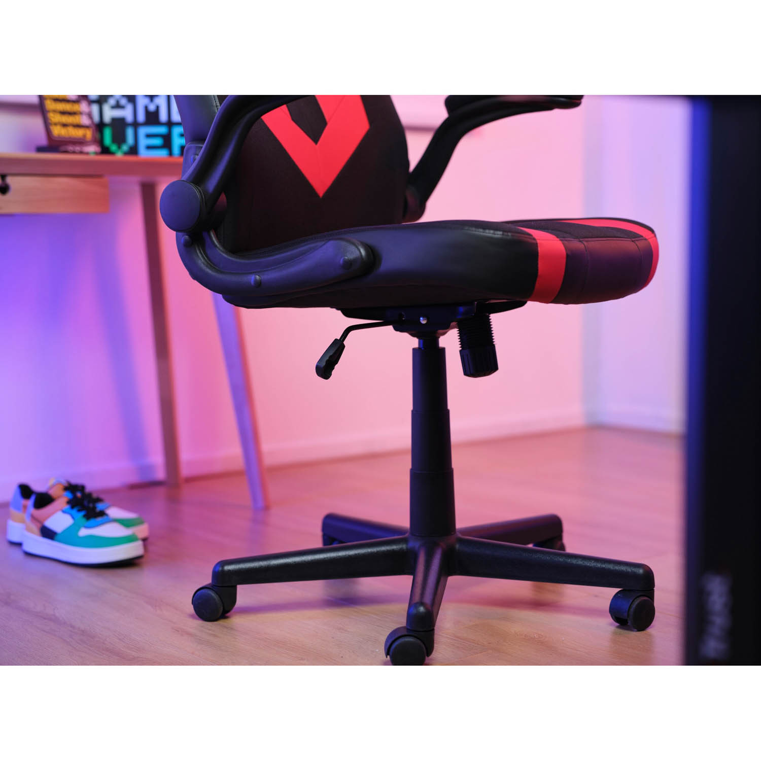 Sedia da gaming con design rosso e nero. Base nera con ruote e scrivania con scarpe.
