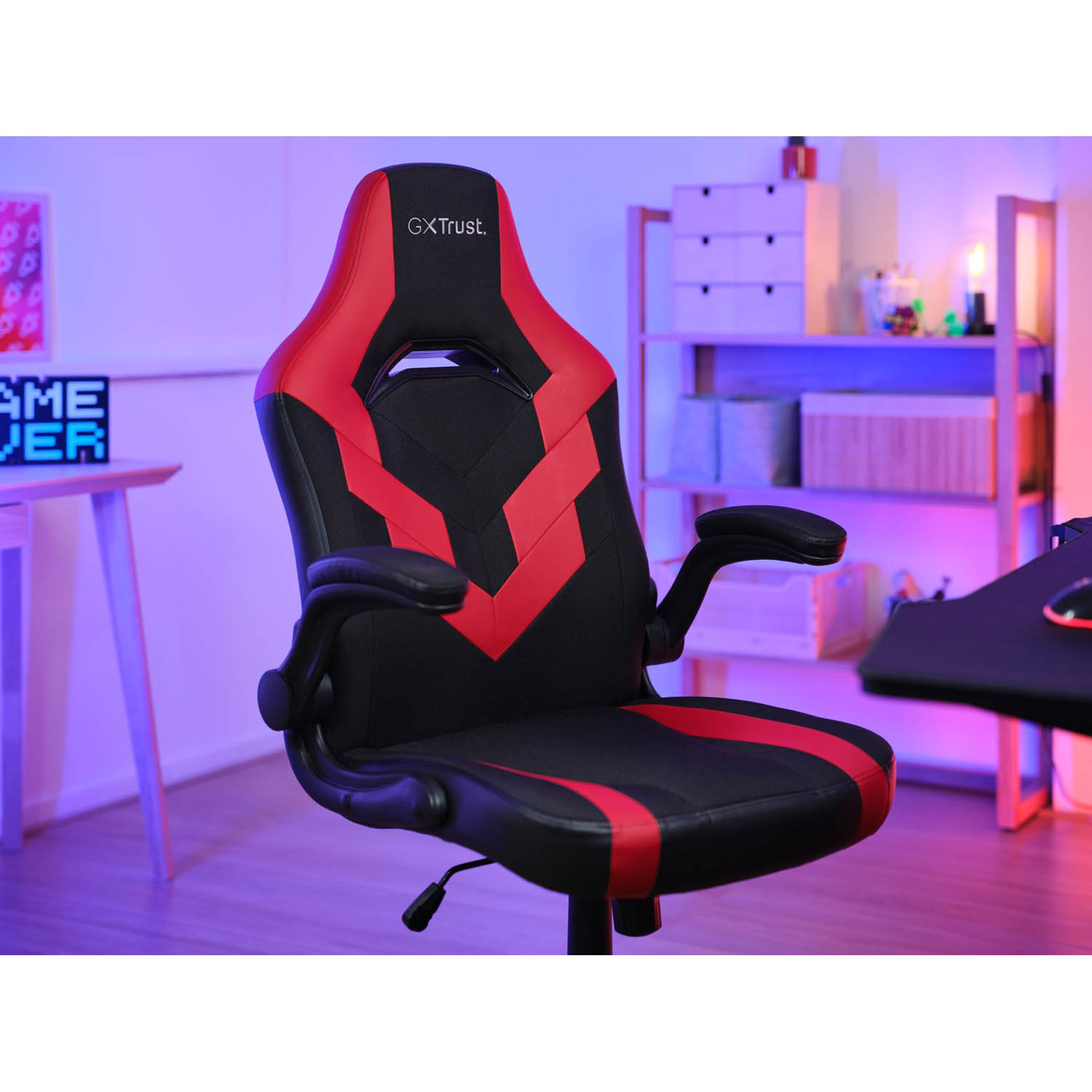 Sedia da gaming: nera e rossa con braccioli. Sfondo: scrivania, monitor e scaffale.