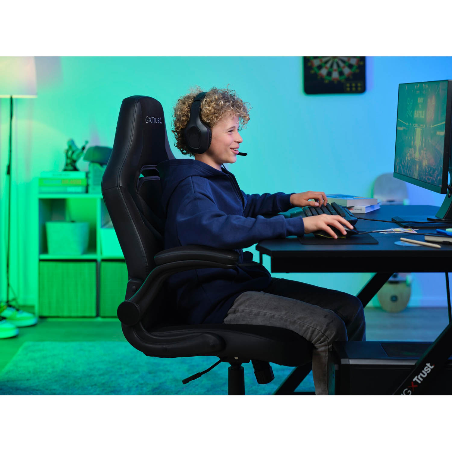 Un ragazzo su una sedia da gioco usa un computer. Indossa le cuffie e guarda lo schermo.