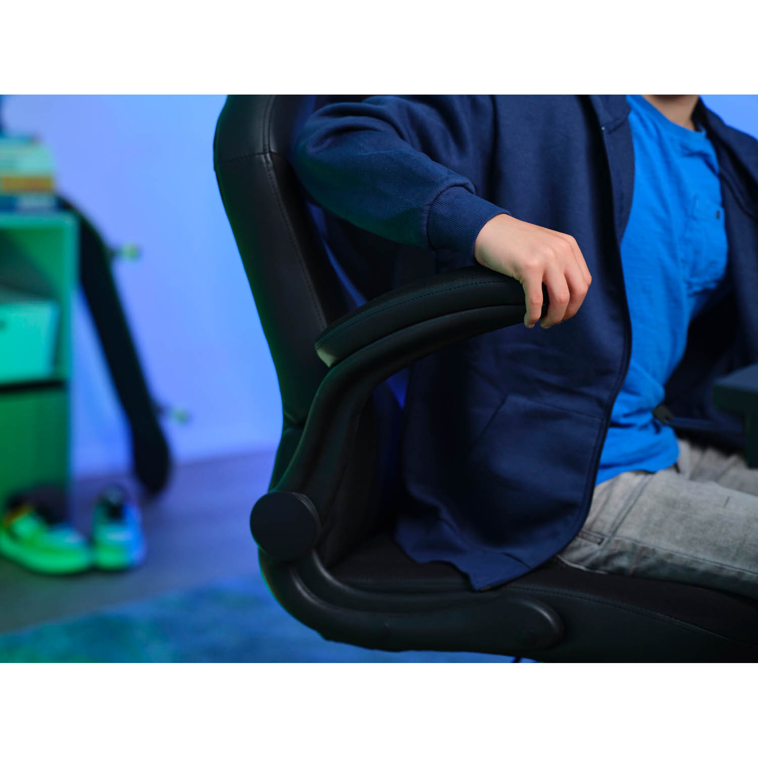 Una persona è seduta su una sedia da gioco nera, giacca blu e pantaloni grigi.