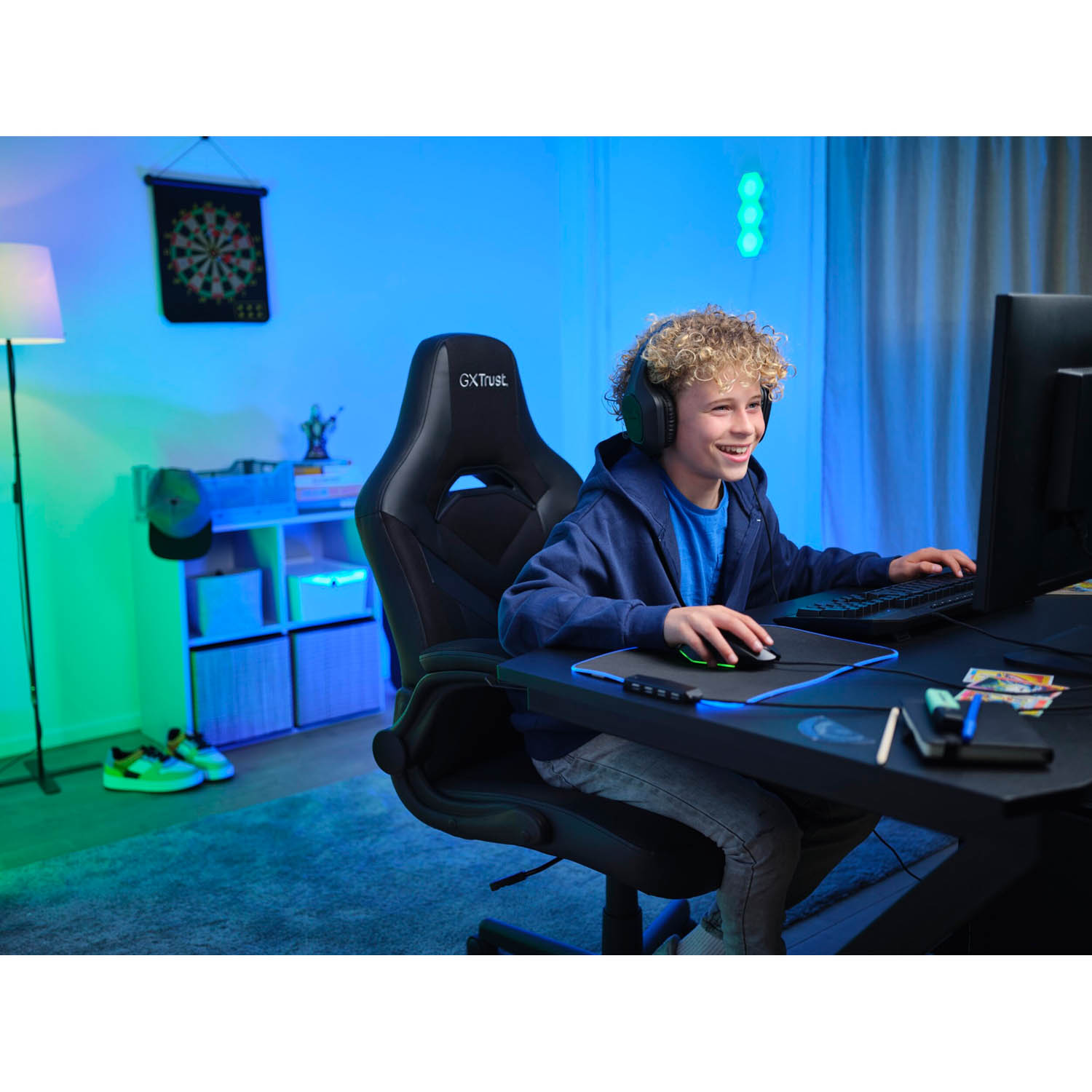 Ragazzo sorridente mentre gioca. Indossa le cuffie, usa un mouse ed è seduto su una sedia da gaming.