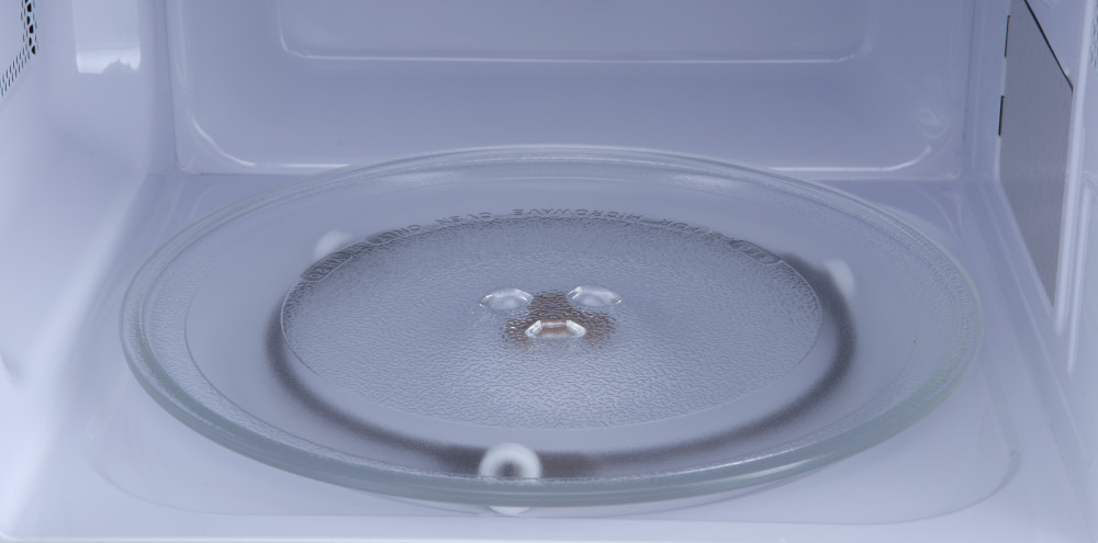 Inside a microwave oven, a clear glass plate rests on a rotating base.