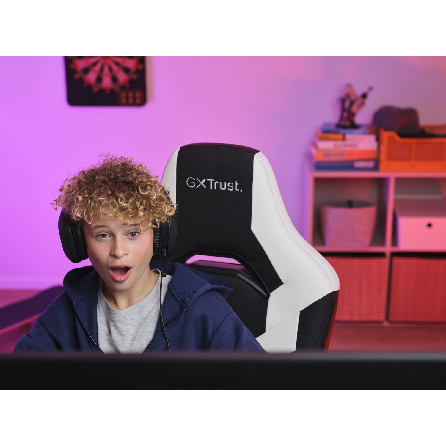 Un ragazzo con cuffie e sedia da gaming, che sembra sorpreso, con un setup di gioco sullo sfondo.