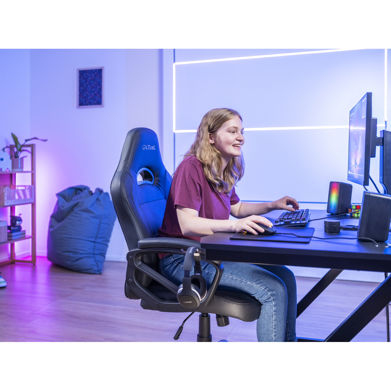Donna sorridente mentre gioca al computer con cuffie e sedia da gioco.