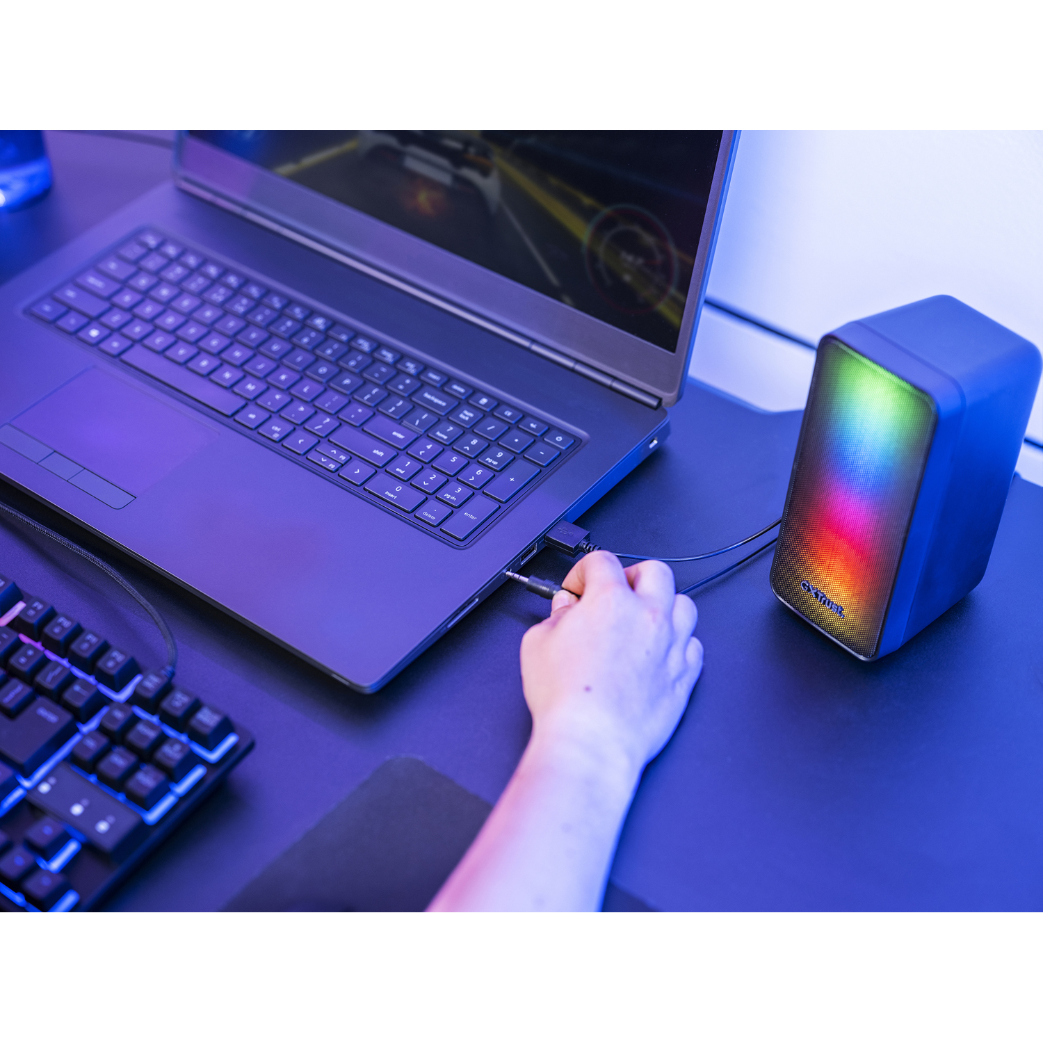 Laptop collegato a un altoparlante con luci colorate, con tastiera e mouse visibili.