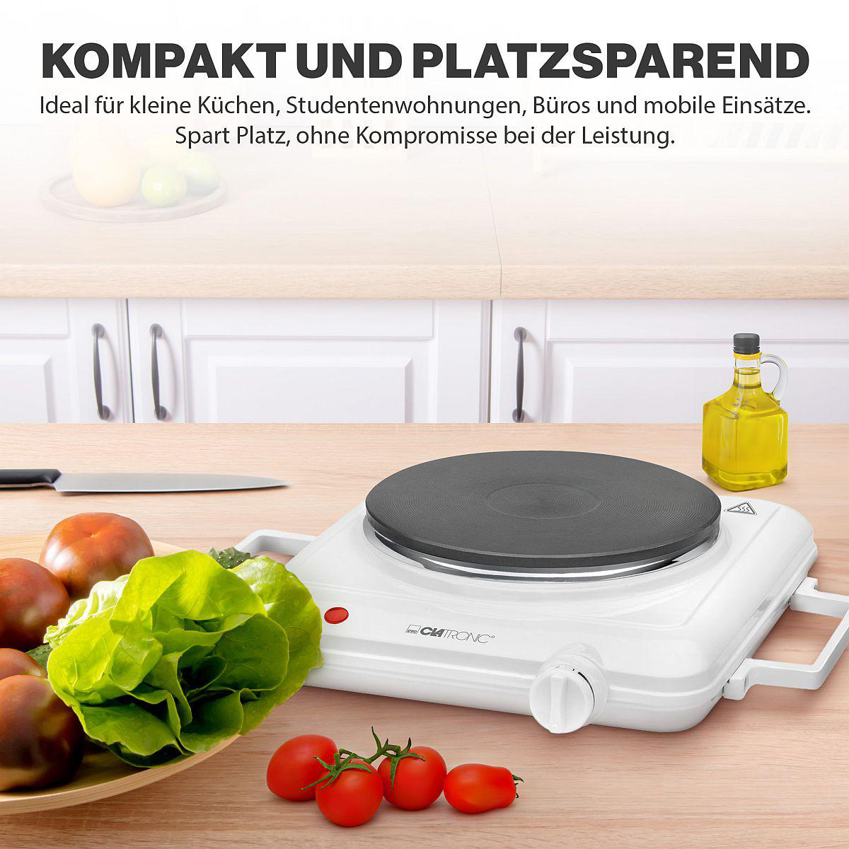 Weißes elektrisches Kochfeld mit schwarzer Kochfläche, Tomatenteller und Gemüse.