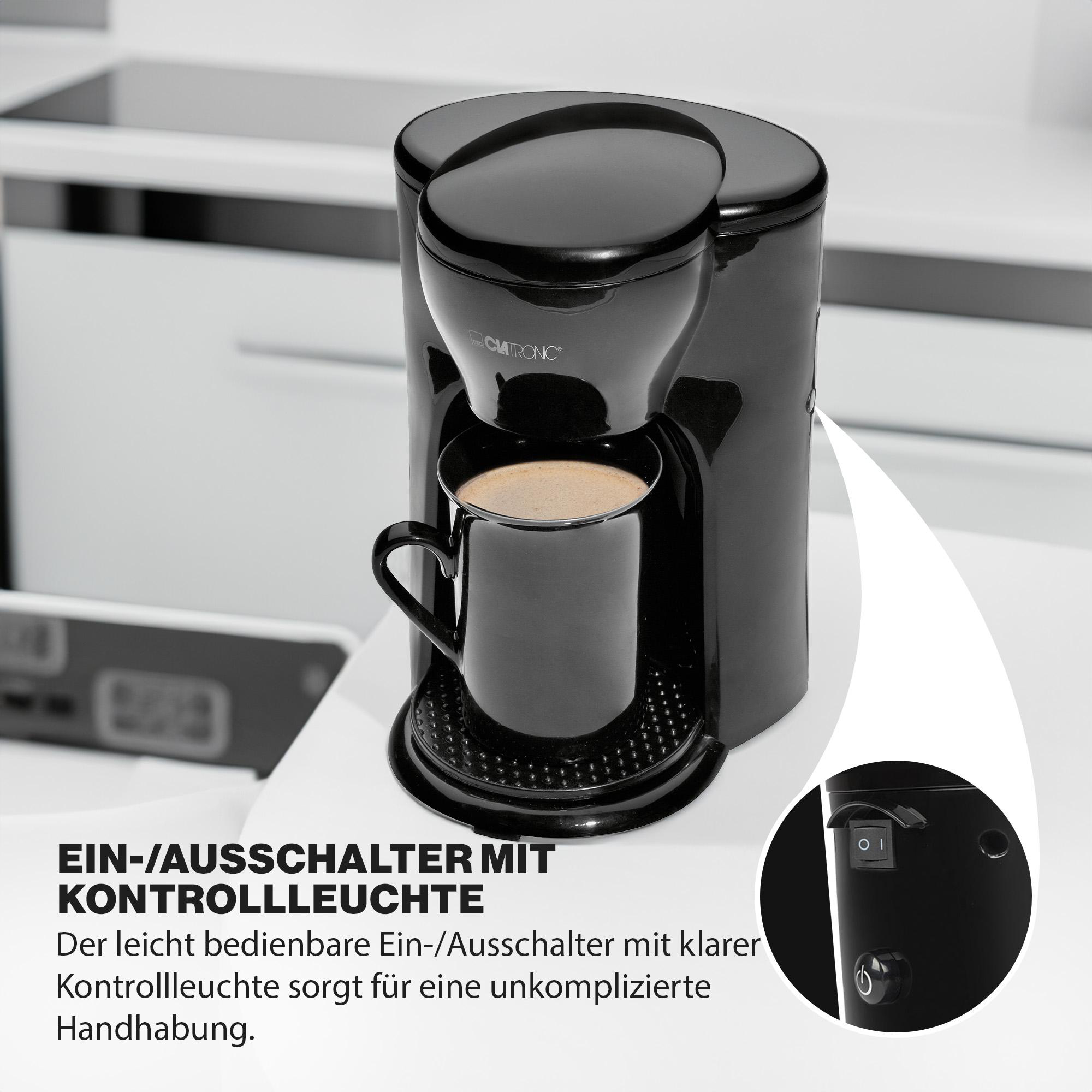 Schwarze Kaffeemaschine mit schwarzer Tasse, Nahaufnahme des Ein-/Ausschalters und Text auf Deutsch.