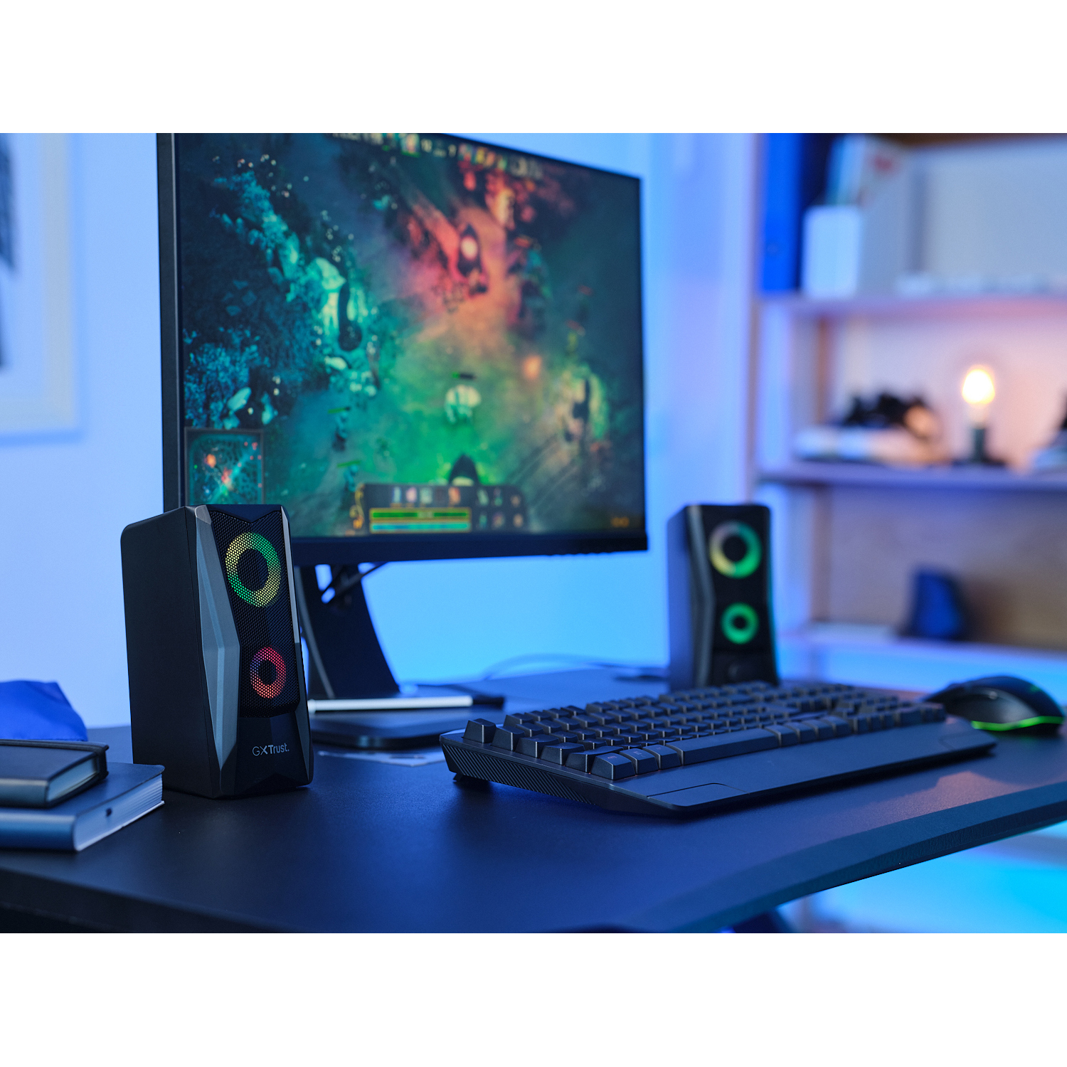 Altoparlanti su una scrivania con un monitor che mostra un gioco. Tastiera, mouse e altri oggetti.