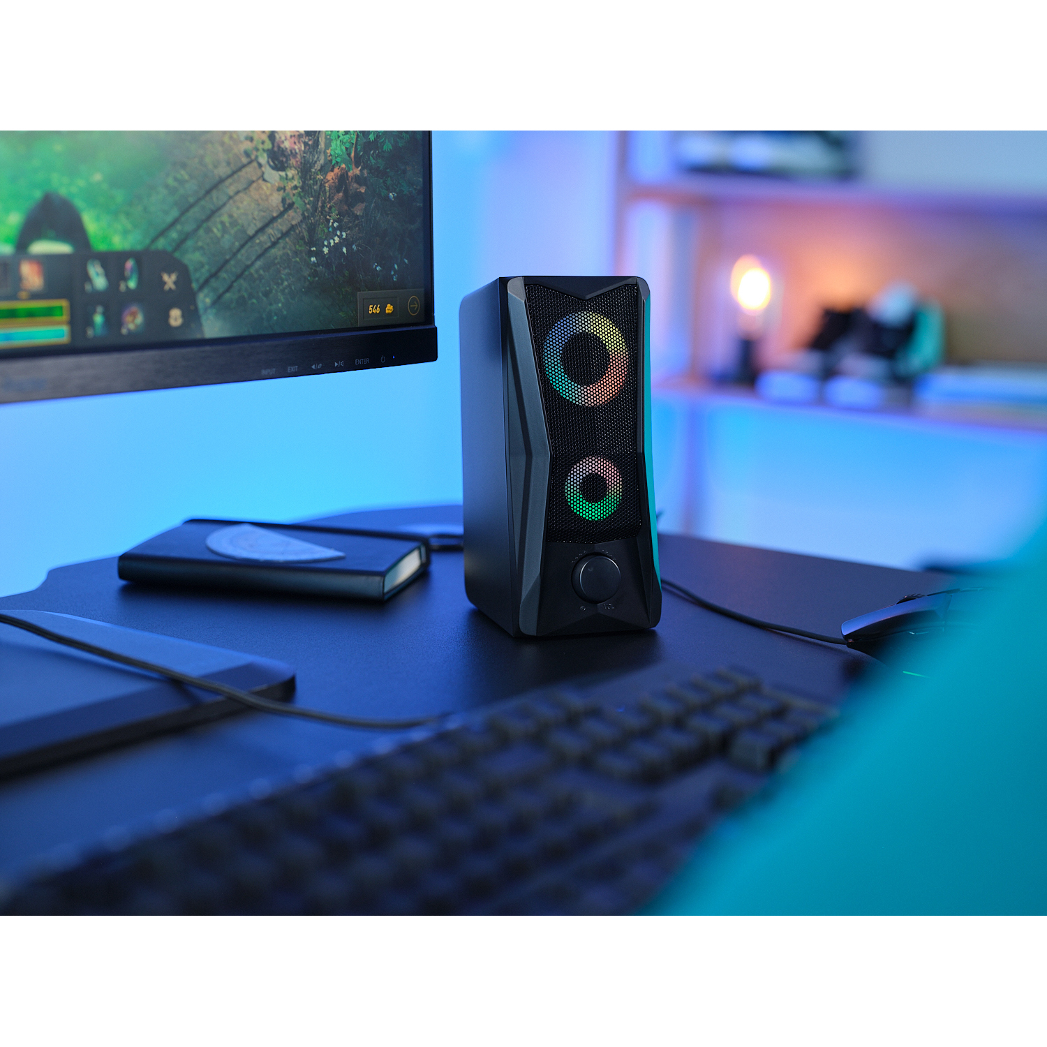 Altoparlante per computer nero con cerchi colorati su una scrivania con monitor, tastiera e altri oggetti.
