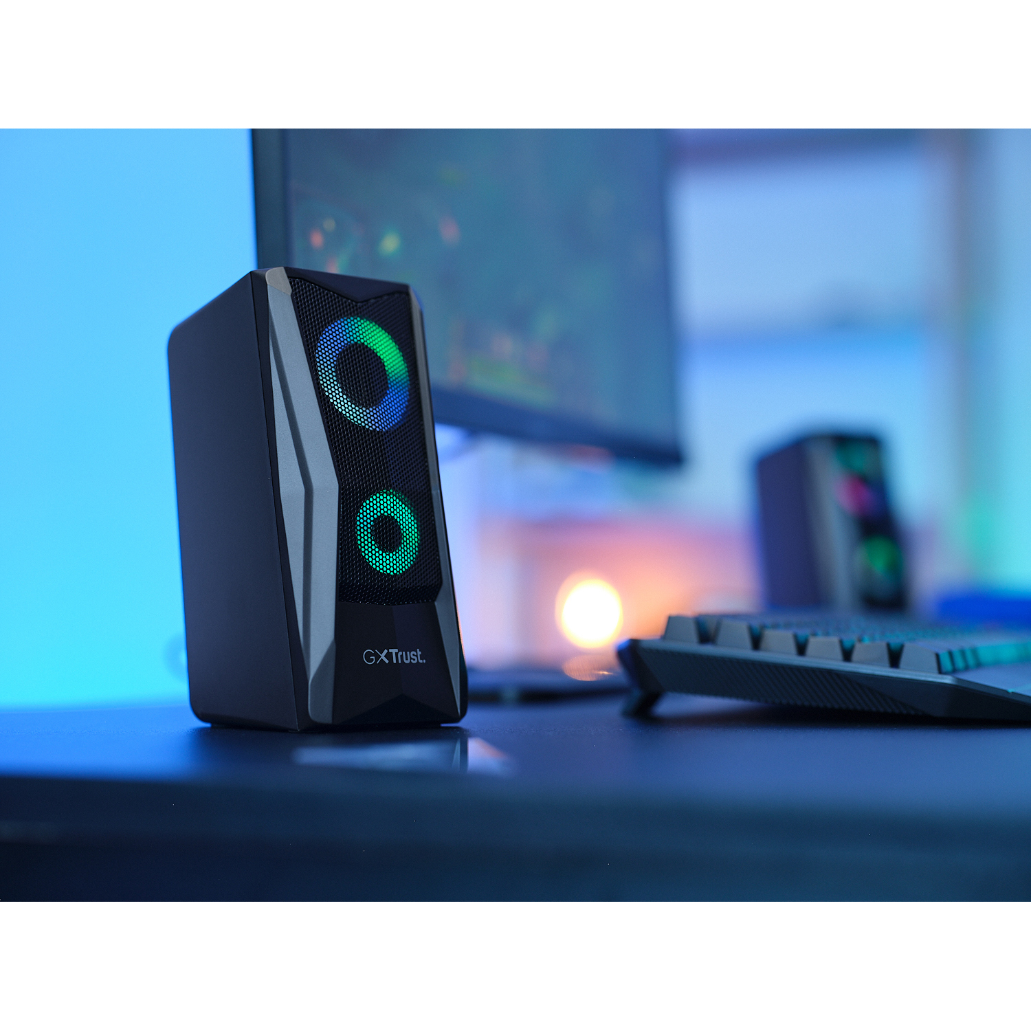 Un altoparlante nero con due luci circolari, con una tastiera e un monitor sullo sfondo.