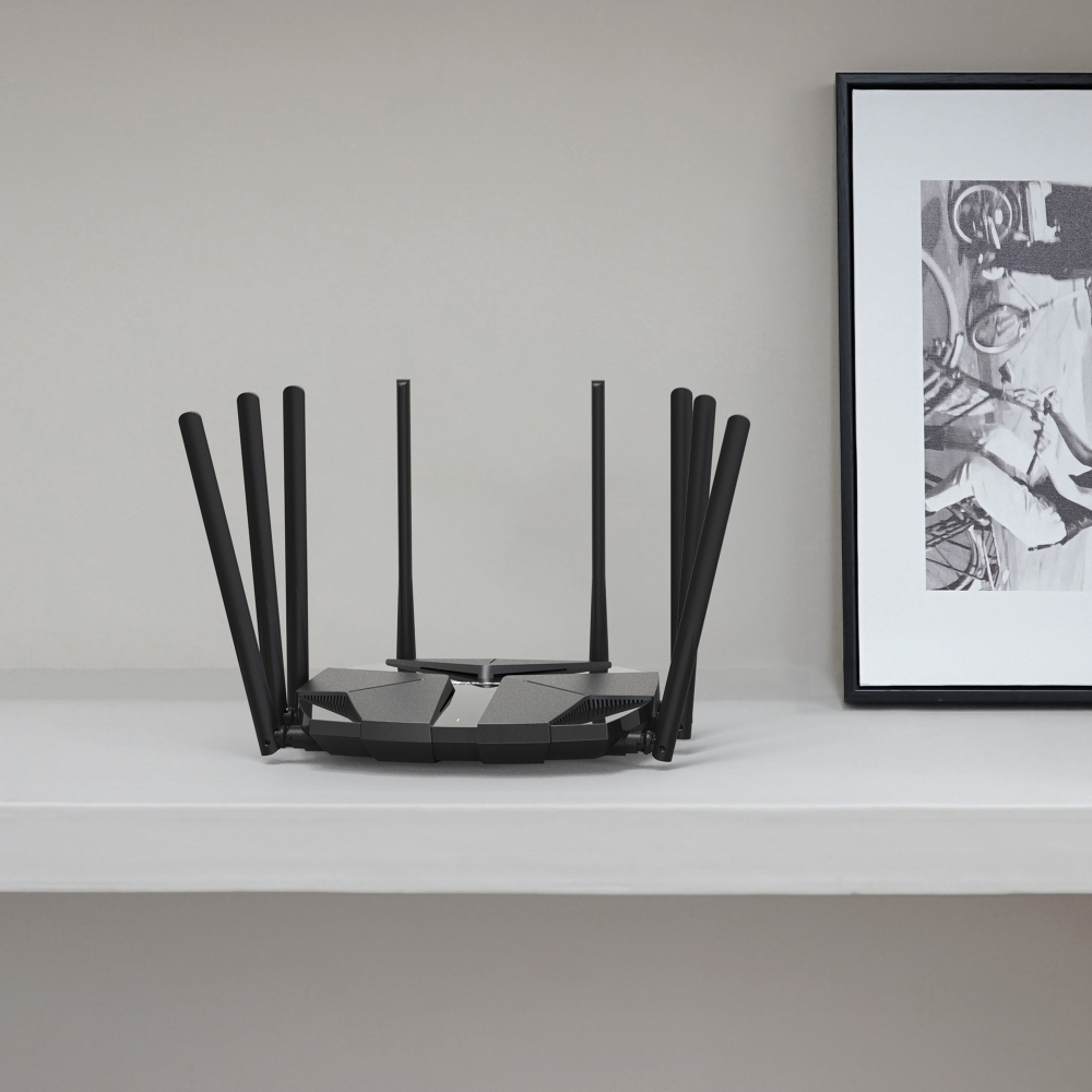 Fekete router antennákkal fehér polcon. Mögötte egy fekete-fehér képkeret.